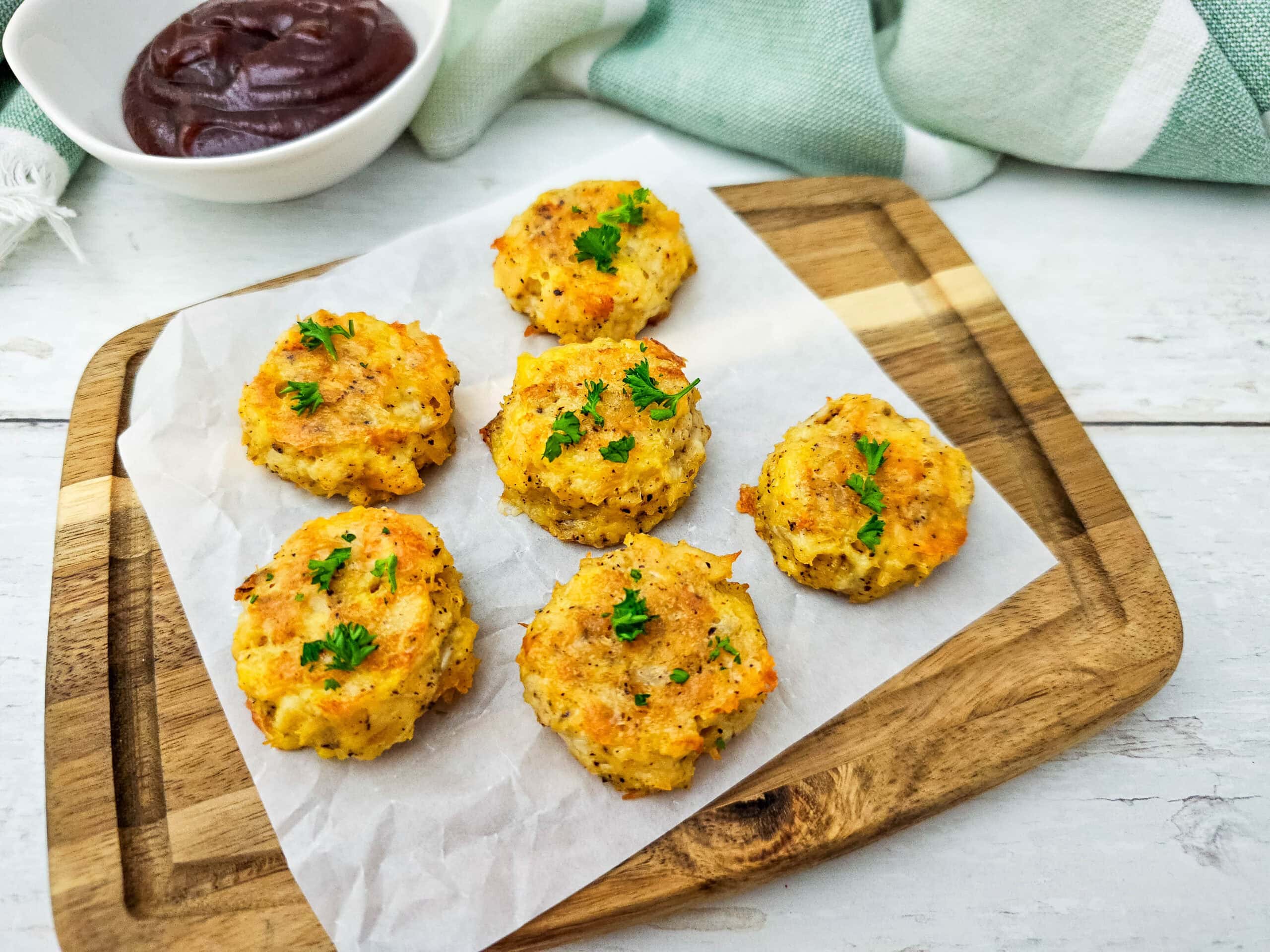 Overhead shot of bite-sized low carb chicken nuggets arranged neatly on a wooden board, served with a small bowl of dipping sauce.