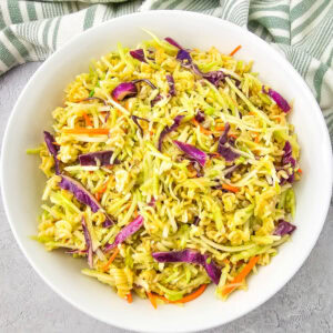 Bright overhead image of Ramen Noodle Broccoli Slaw Salad in a white bowl, with vibrant red cabbage, shredded carrots, and crushed noodles visible throughout.
