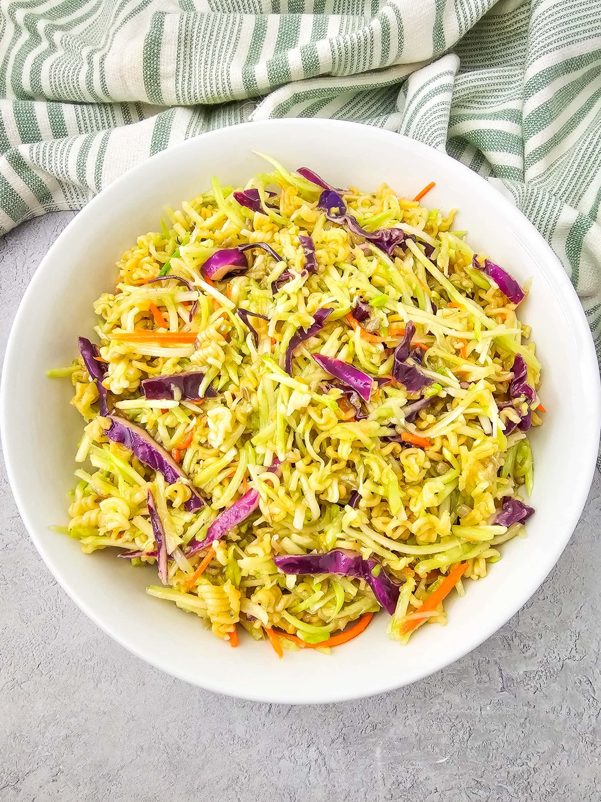 Bright overhead image of Ramen Noodle Broccoli Slaw Salad in a white bowl, with vibrant red cabbage, shredded carrots, and crushed noodles visible throughout.