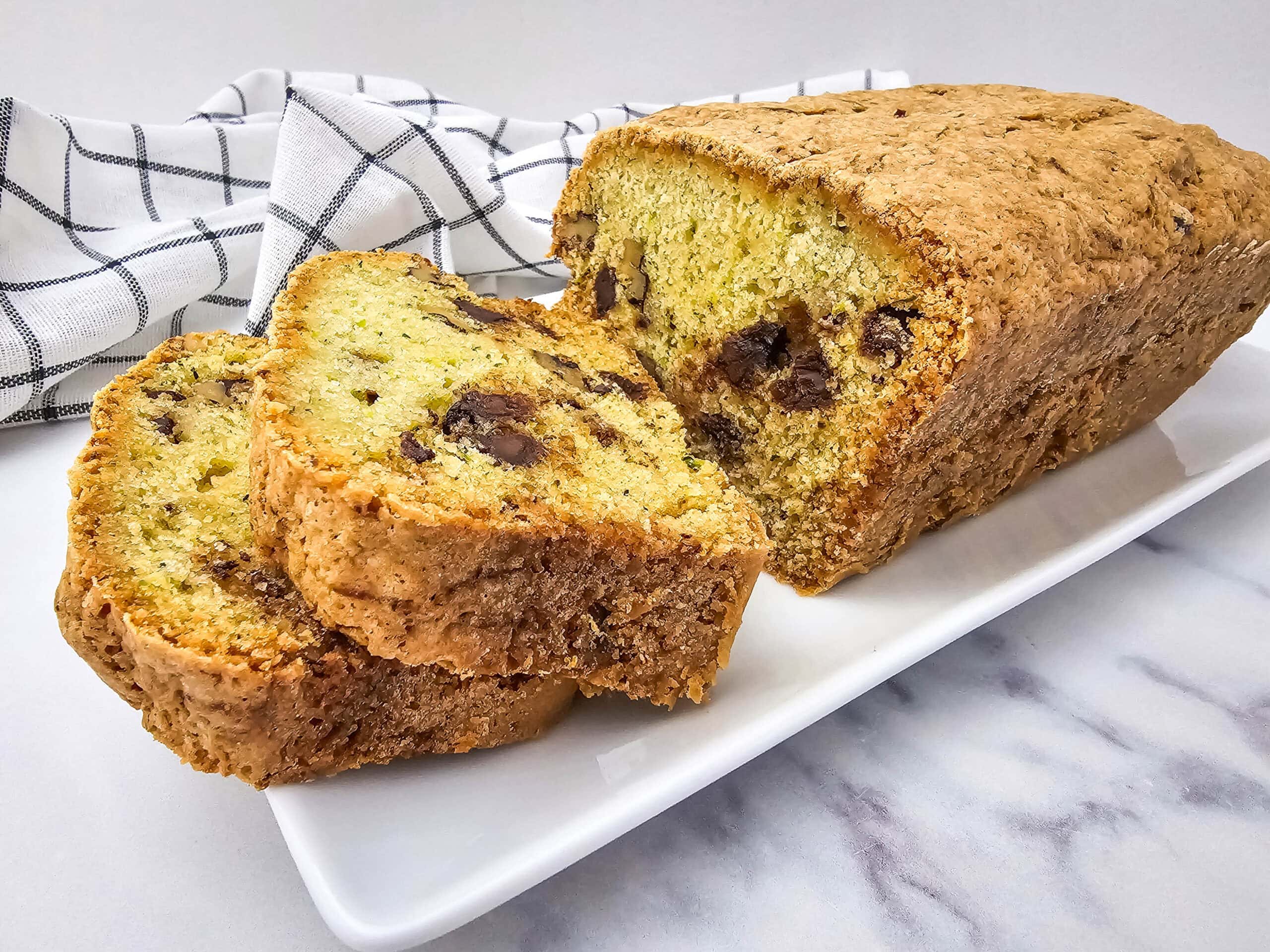 Side view of a loaf of walnut and chocolate chip zucchini bread with two slices stacked slightly, highlighting its golden crust and rich filling.