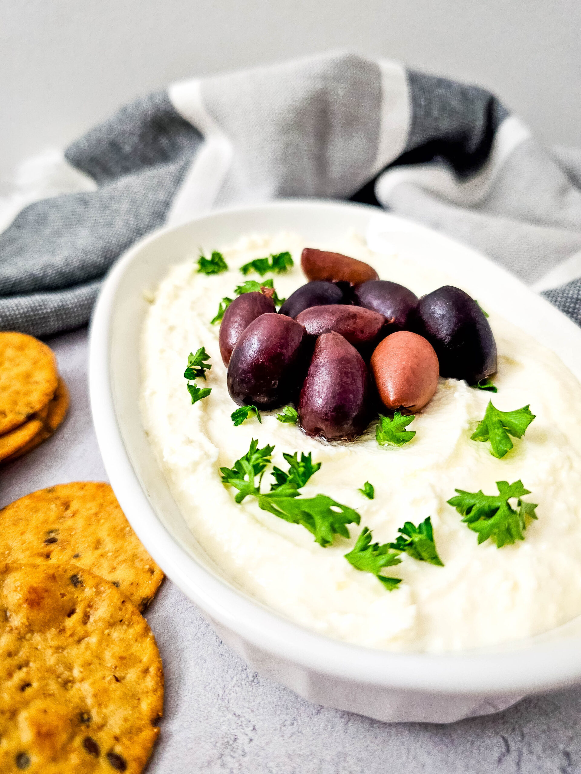 Side view of whipped feta dip showing a fluffy, creamy texture, garnished with olives and parsley, ready to be served with crackers.