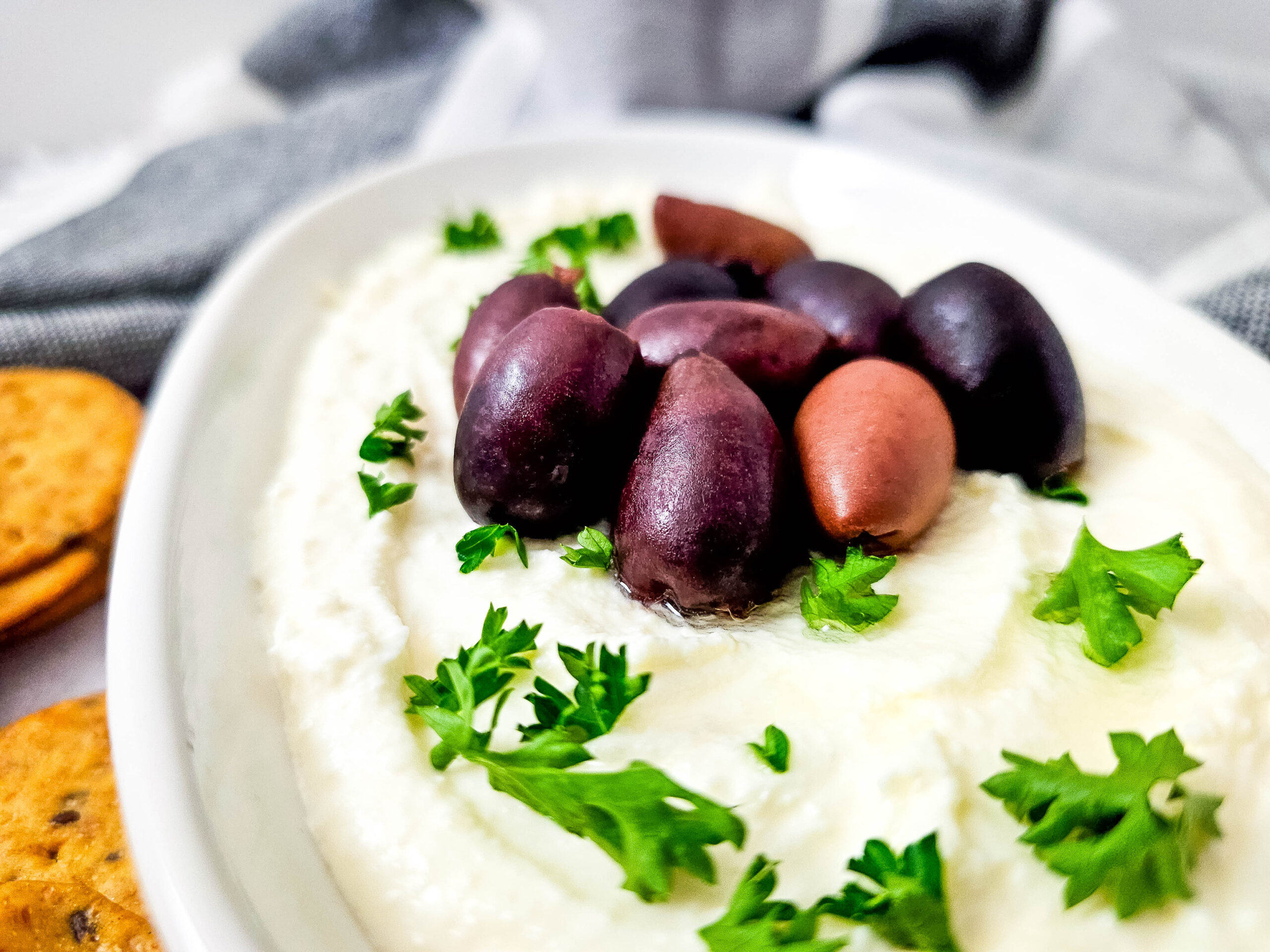 Close-up shot highlighting the creamy texture of whipped feta dip with Kalamata olives and fresh parsley sprinkled on top.