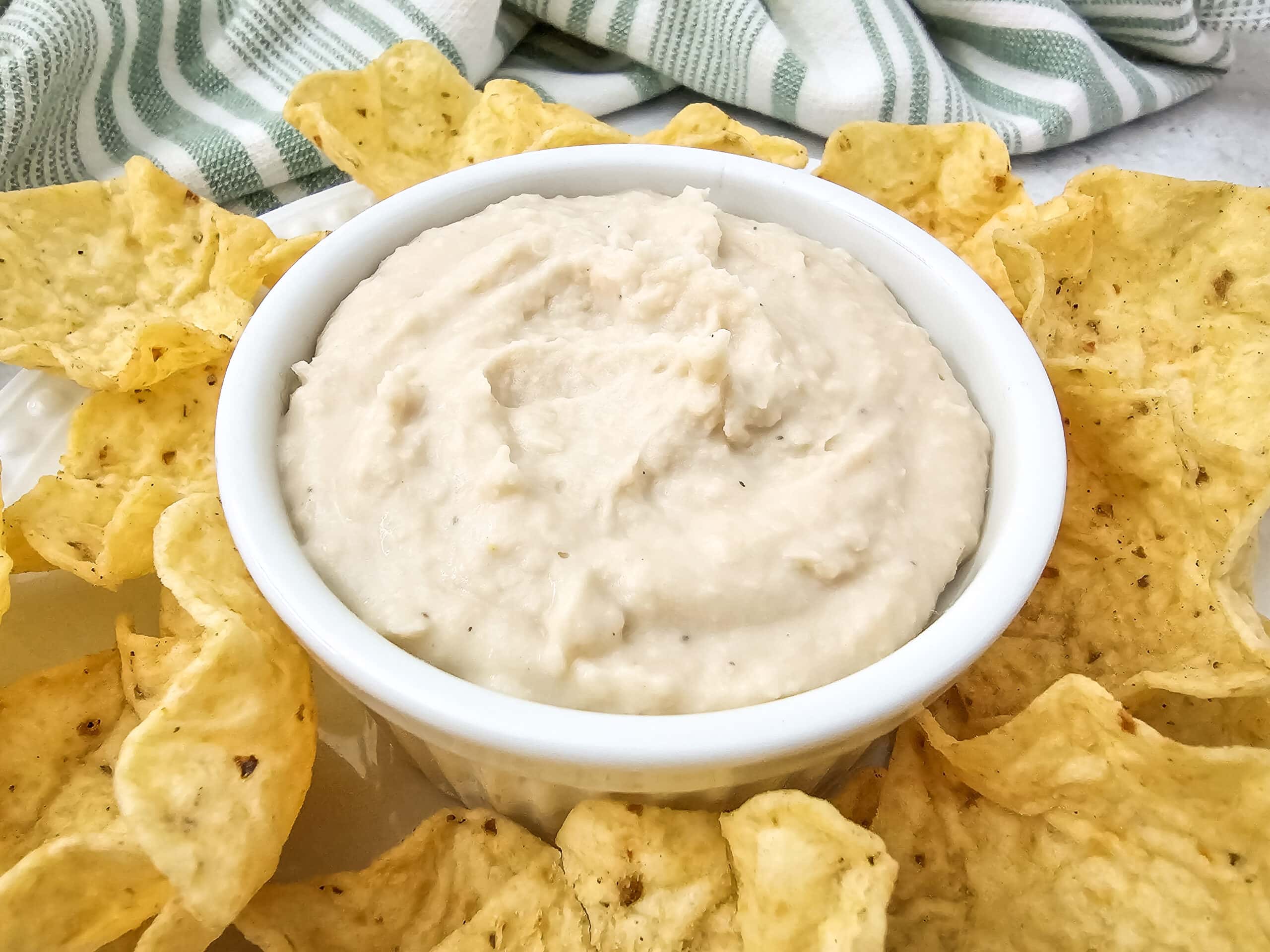 Angled shot of white bean dip showing its creamy texture, surrounded by crunchy tortilla scoop chips.