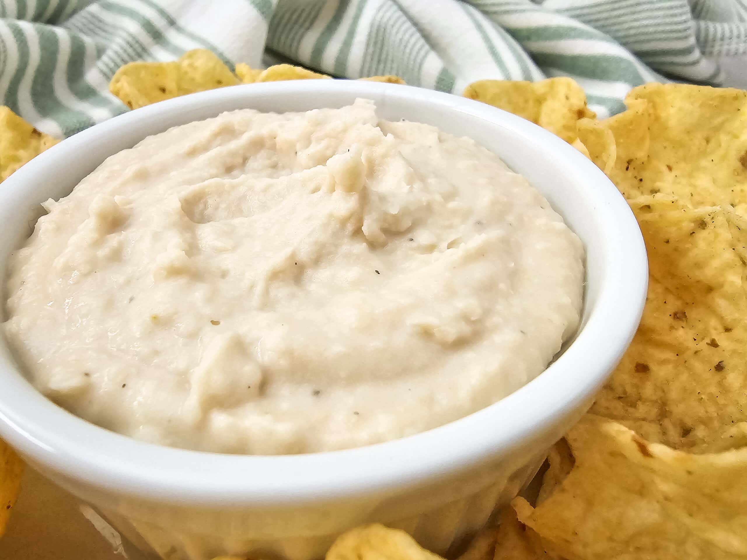 Close-up shot highlighting the smooth consistency of white bean dip with tortilla chips arranged around the serving bowl.
