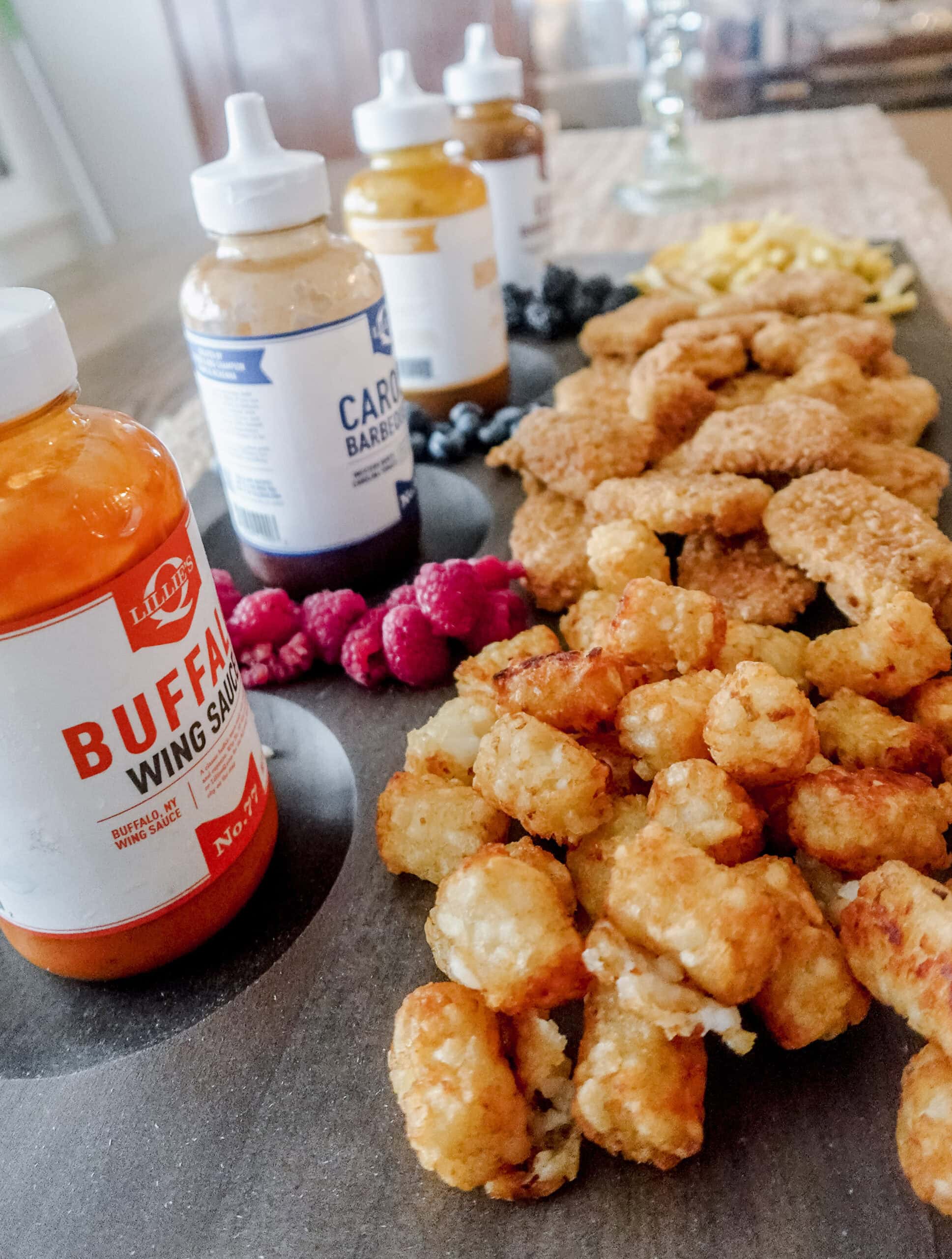 A food board featuring crispy chicken nuggets, golden tater tots, fresh berries, and dipping sauces including buffalo, Carolina barbecue, honey gold, and gold barbecue.