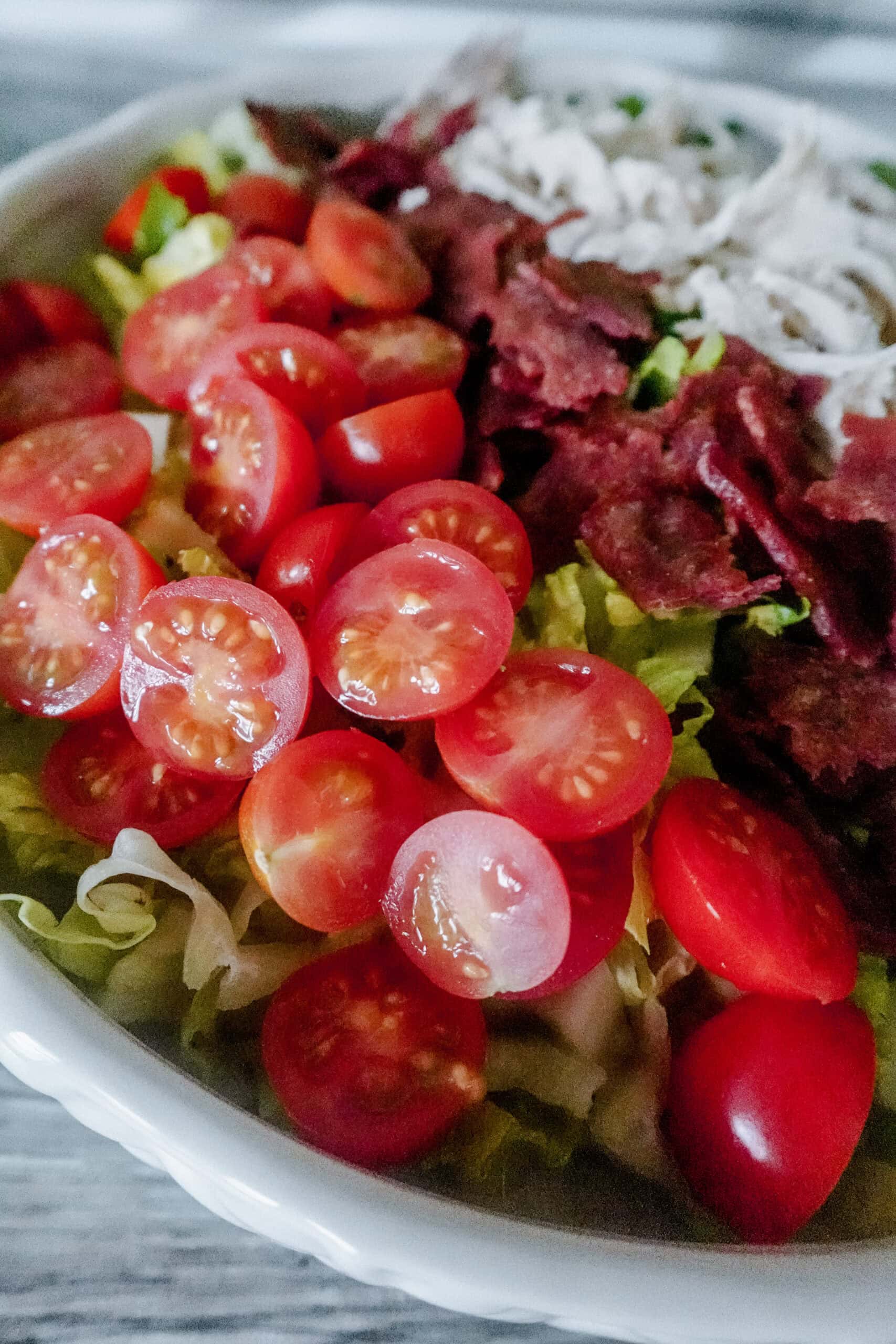 Bright red halved cherry tomatoes piled next to crispy bacon pieces and shredded chicken on a bed of lettuce.