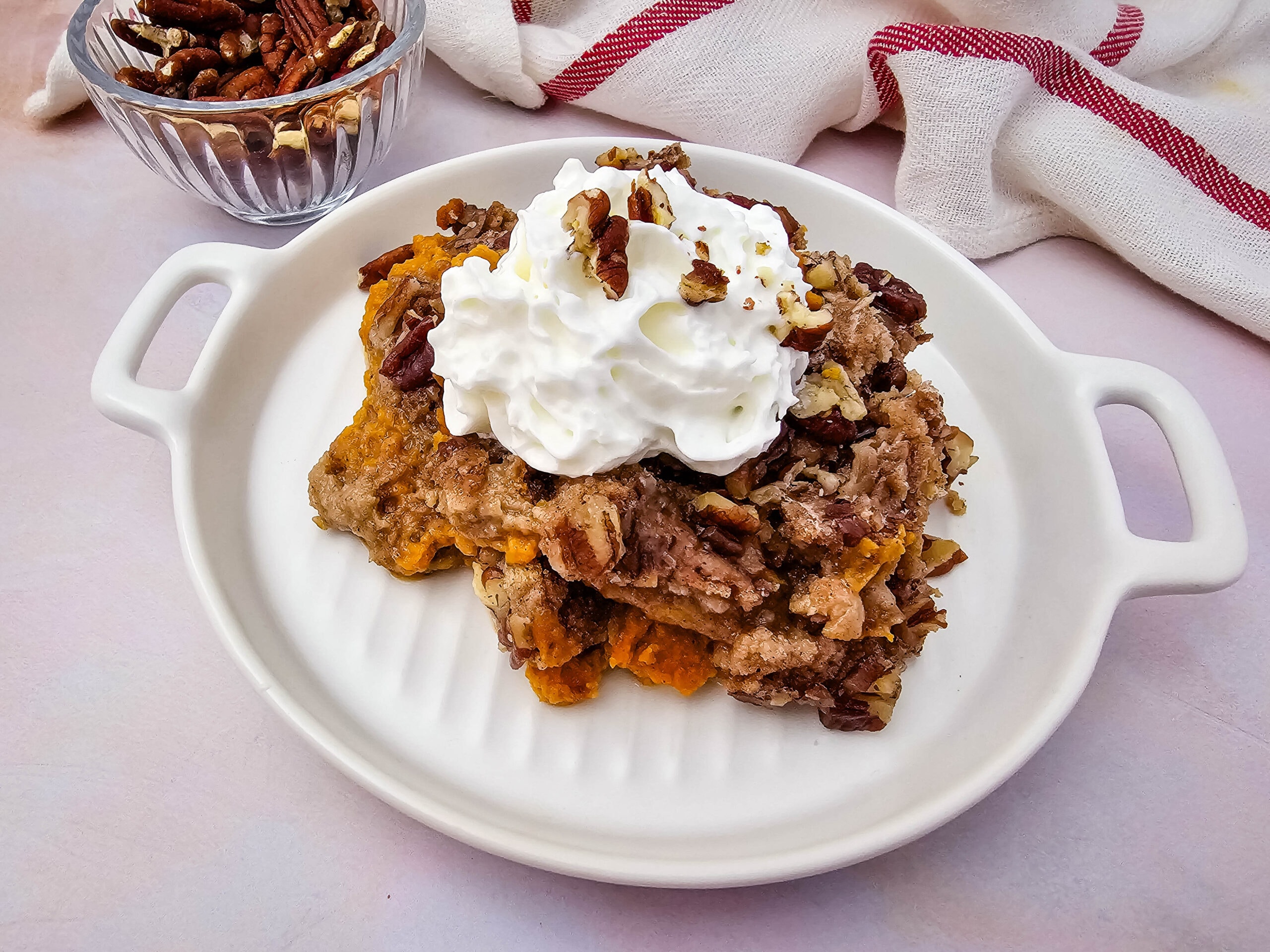 A serving of pumpkin dump cake with whipped cream and pecans on a white plate, photographed from above.