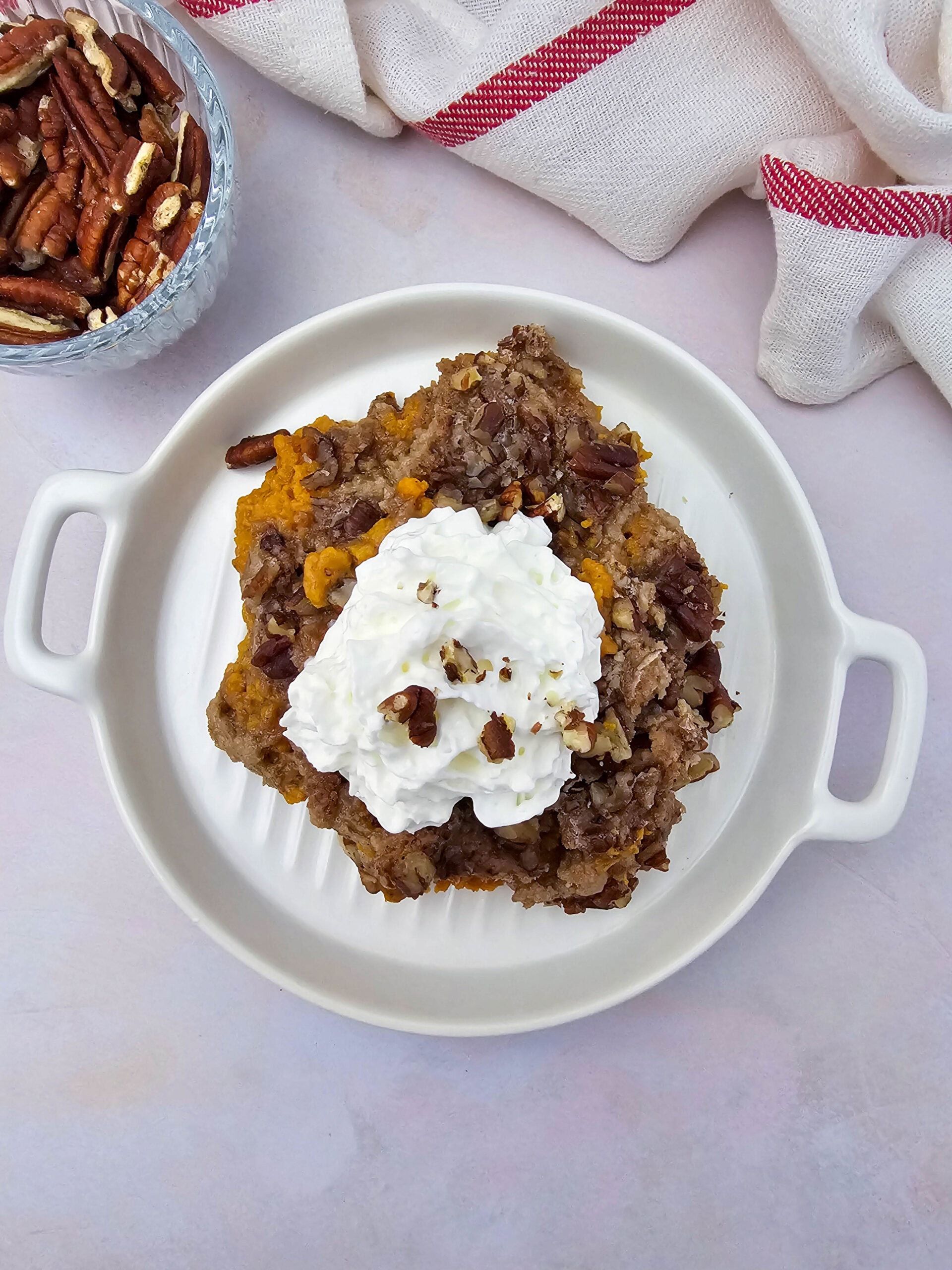 A warm serving of crockpot pumpkin dump cake garnished with whipped cream and chopped pecans, ready to eat.