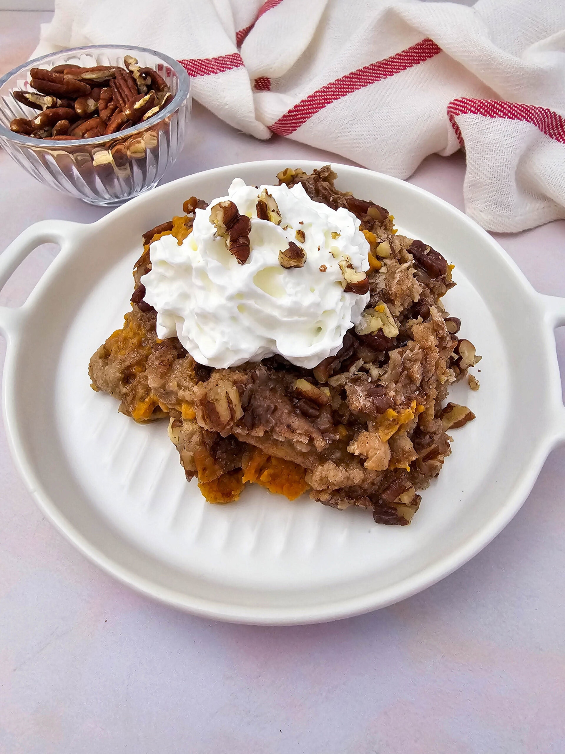 A thick slice of crockpot pumpkin dump cake showing layers of spiced pumpkin filling and crumbly topping, finished with whipped cream and pecans.