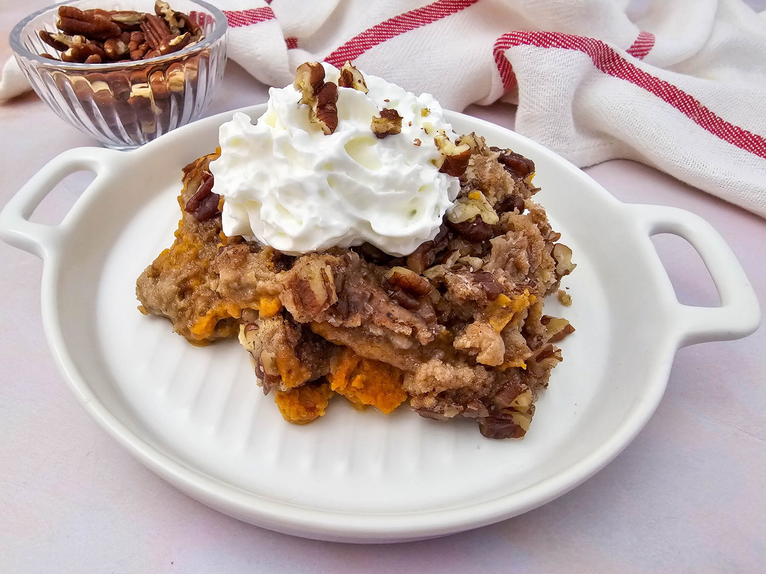 Rich pumpkin dump cake with a crumbly topping, whipped cream, and pecans served on a white dish.