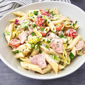 Italian Hoagie Pasta Salad served in a large white bowl, showcasing pasta, deli meat, fresh veggies, and herbs for a colorful, hearty dish.