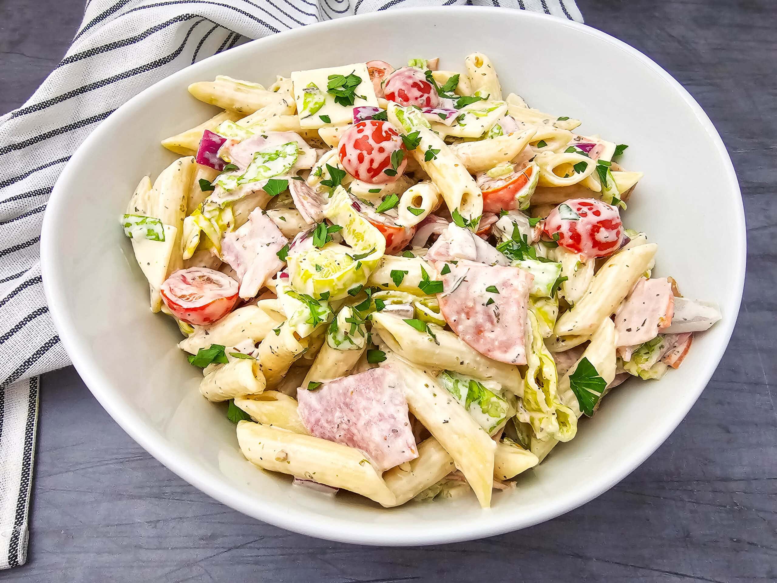 Italian Hoagie Pasta Salad served in a large white bowl, showcasing pasta, deli meat, fresh veggies, and herbs for a colorful, hearty dish.
