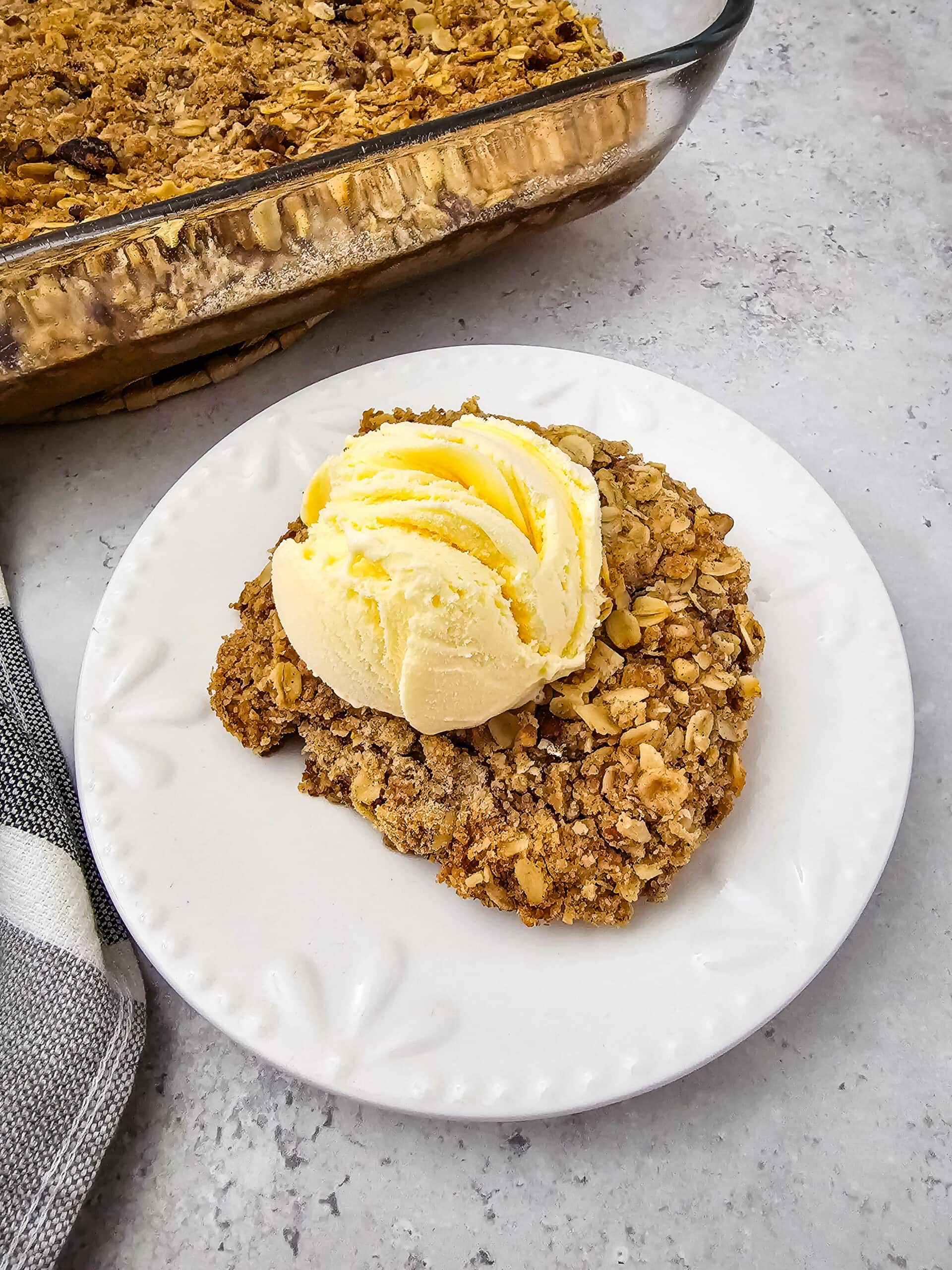 A close-up of a generous piece of pumpkin pie crisp with a crunchy oat topping and creamy scoop of vanilla ice cream.