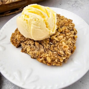A golden-brown oat topping layered over spiced pumpkin filling, served with vanilla ice cream on a white plate.