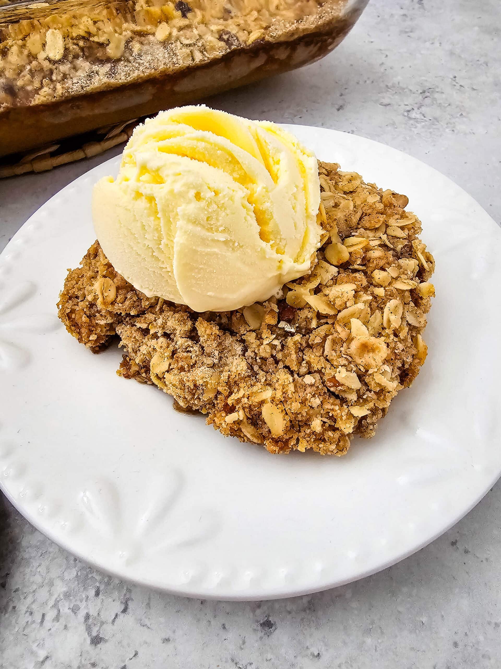 A golden-brown oat topping layered over spiced pumpkin filling, served with vanilla ice cream on a white plate.