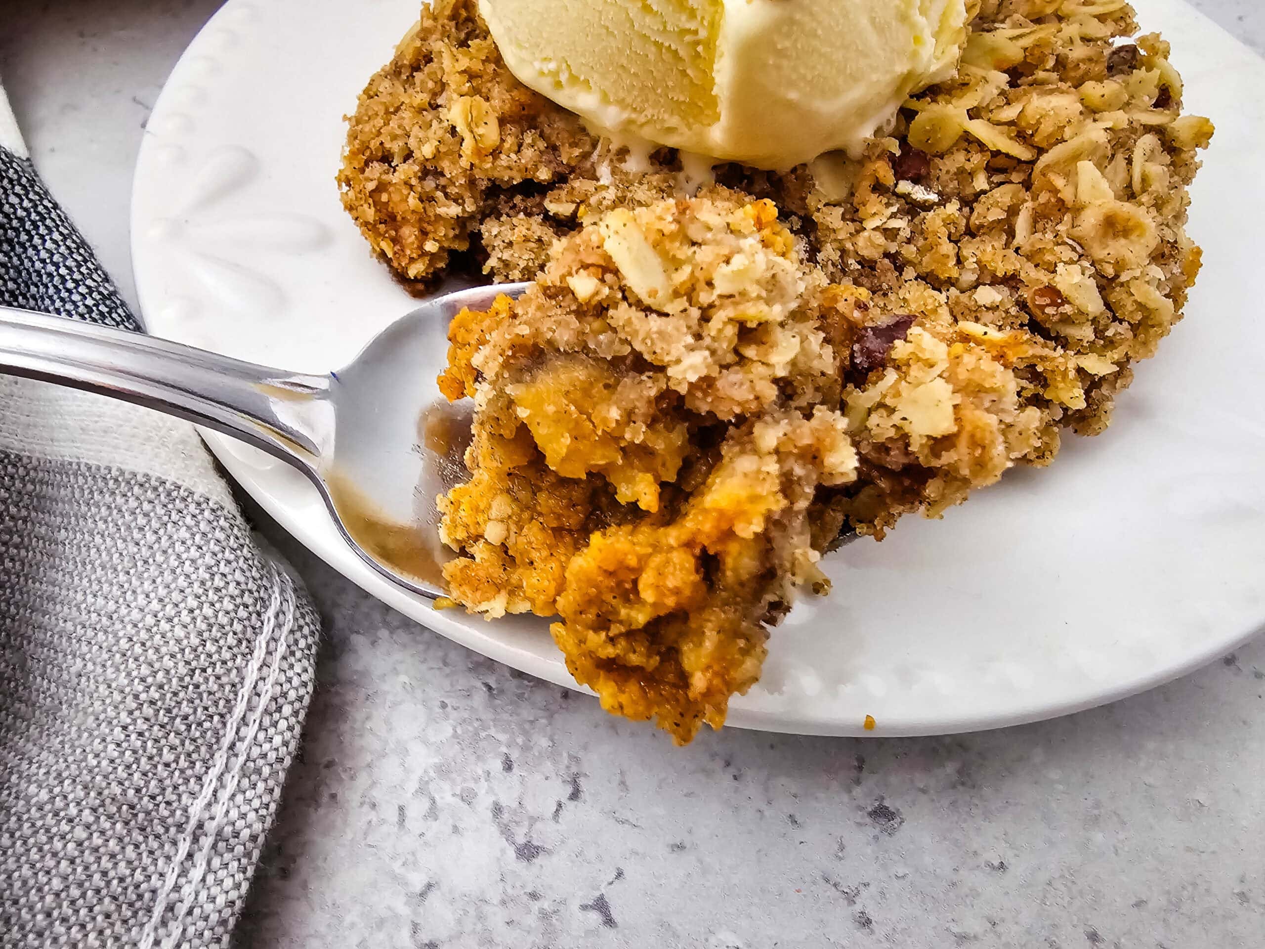 A fork scooping into the spiced pumpkin filling and oat topping, with melting vanilla ice cream on top.