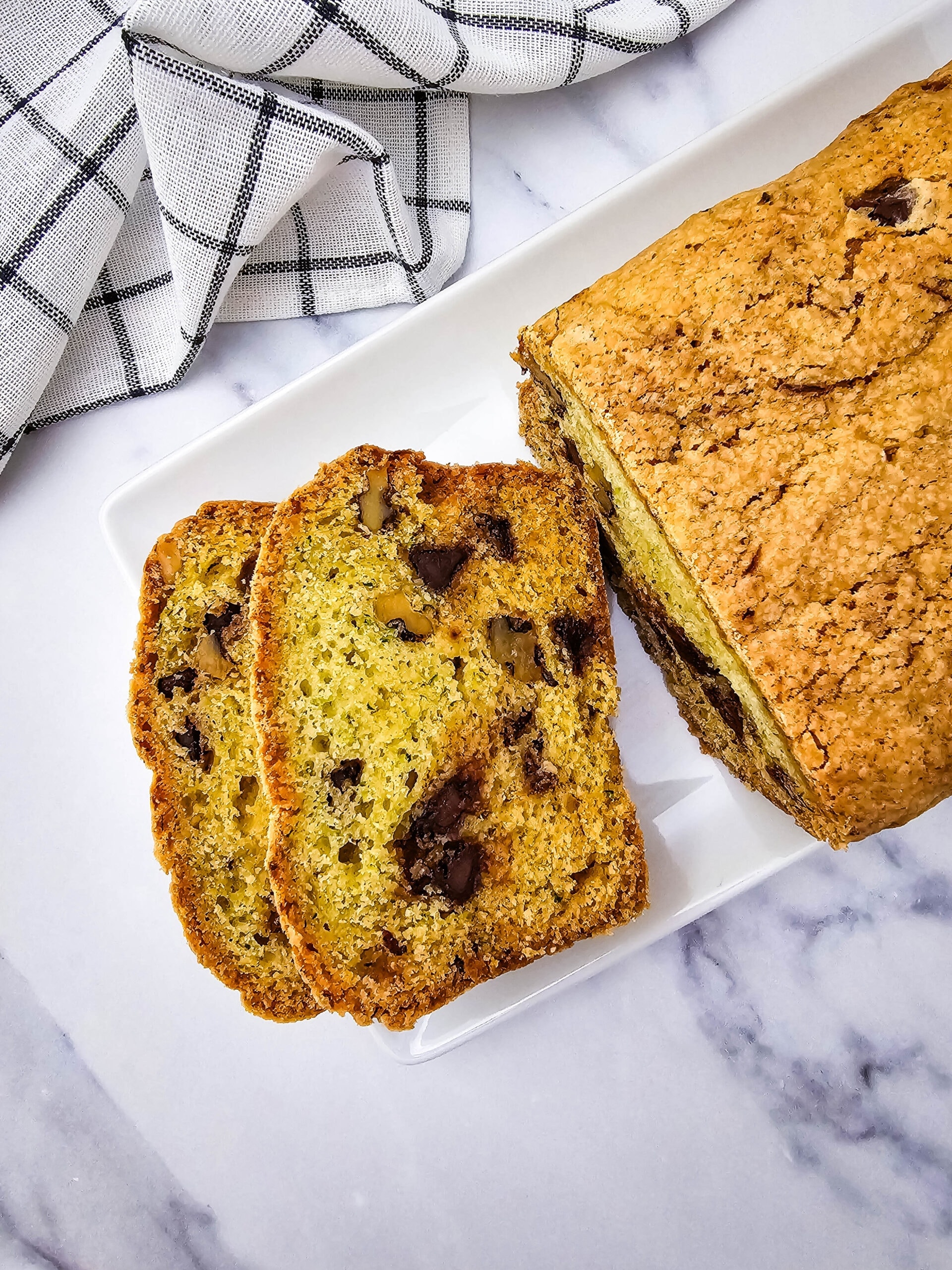 Overhead view of walnut and chocolate chip zucchini bread, partially sliced, with a golden crust and melty chocolate chips visible.