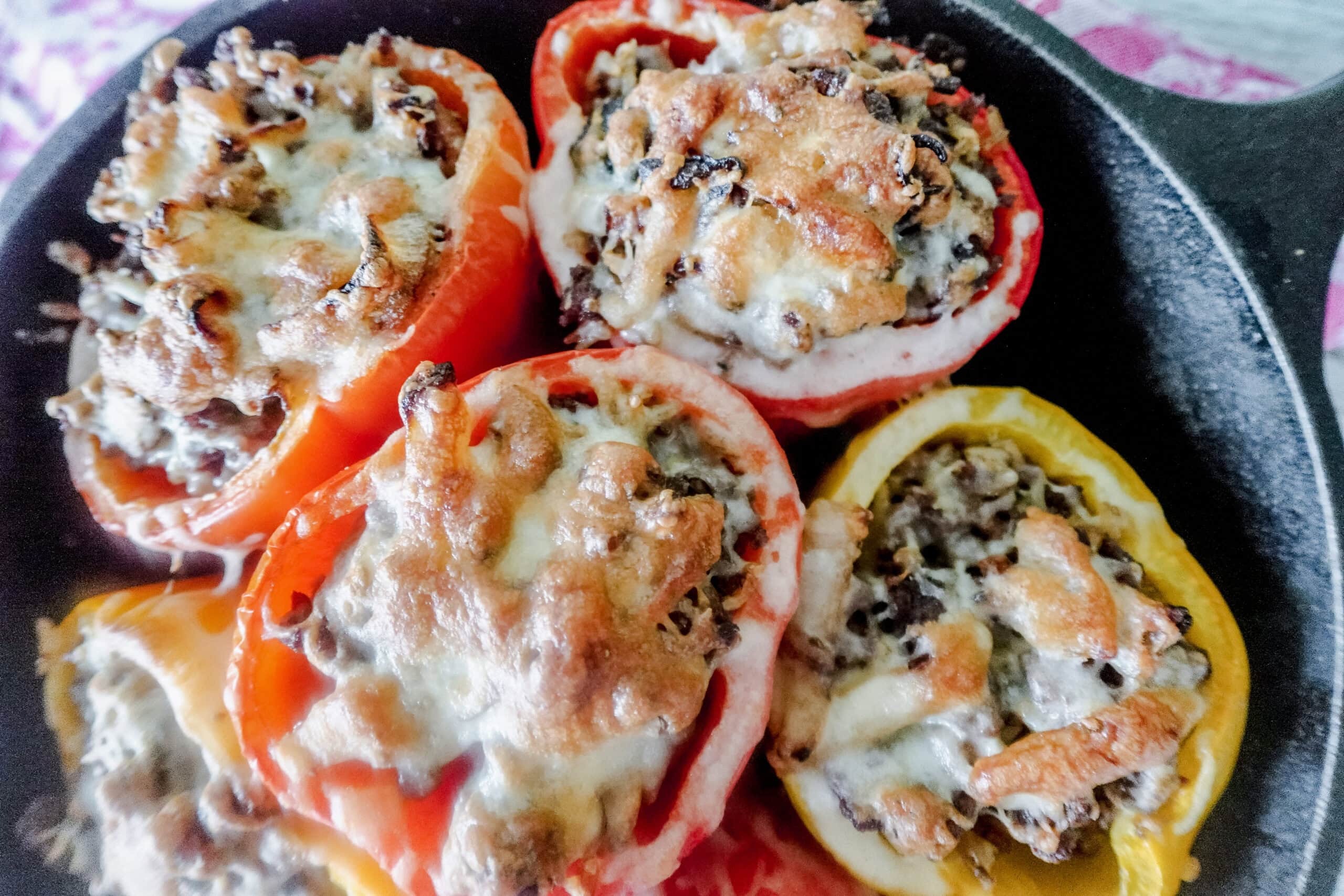 A close up of bright red and yellow stuffed bell peppers in a cast iron skillet. The peppers are filled with a French onion soup beef mixture and topped with brown bubbly cheese.