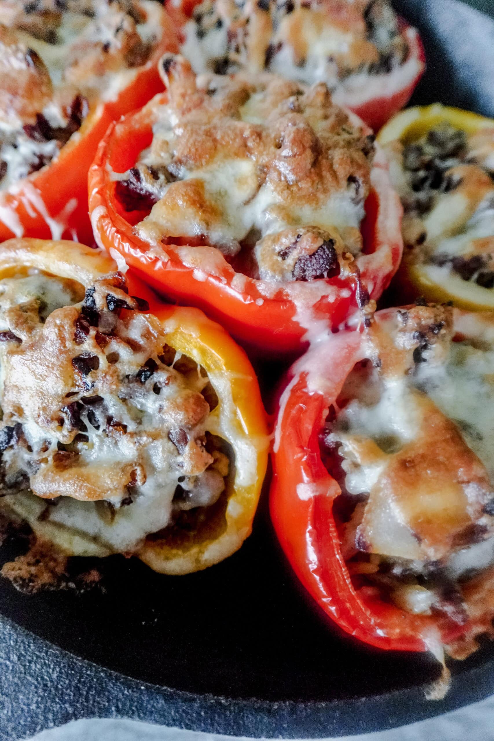A close up of bright red and yellow stuffed bell peppers in a cast iron skillet. The peppers are filled with a French onion soup beef mixture and topped with brown bubbly cheese.