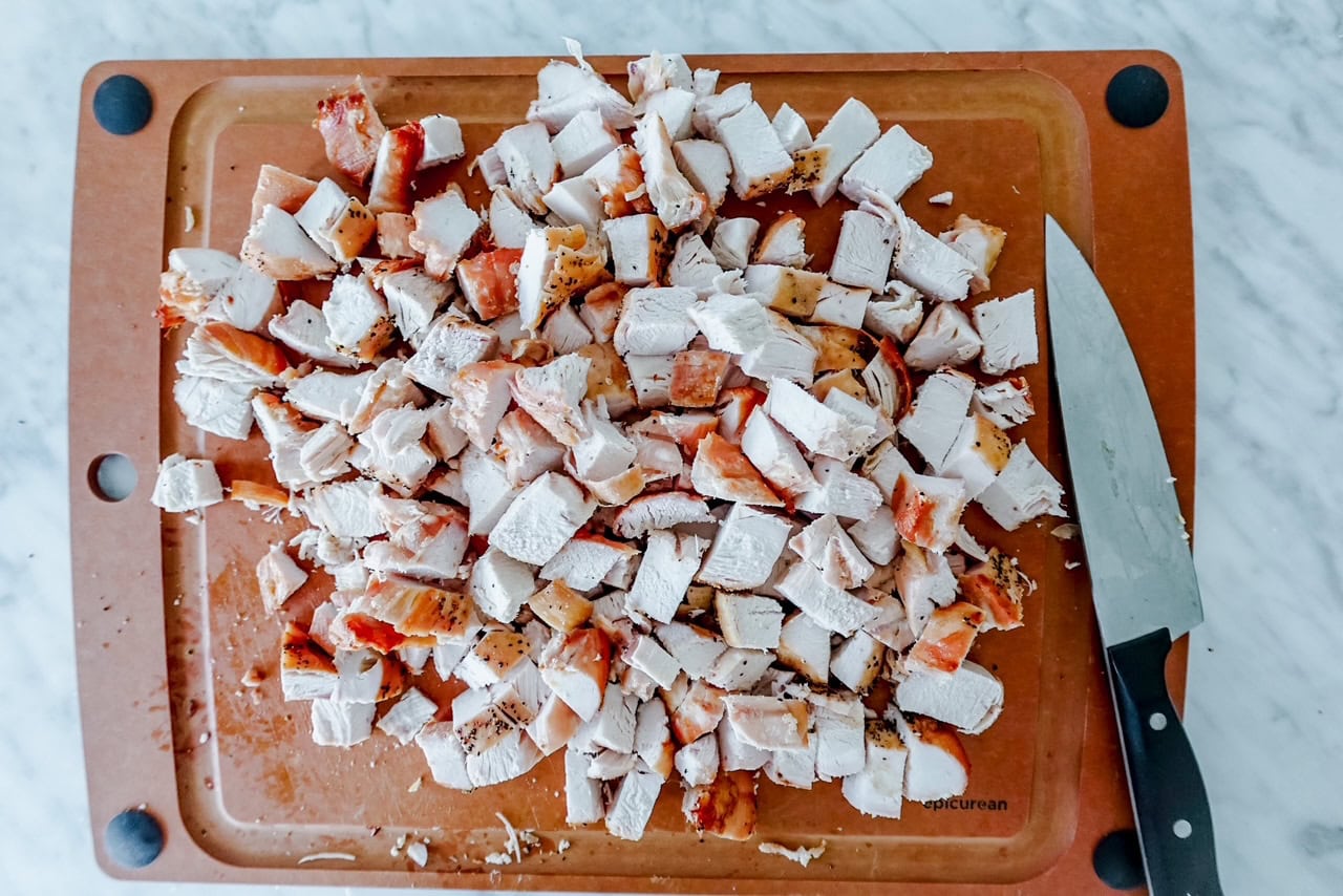 Overhead view of chopped, cooked chicken breast pieces on a cutting board with a knife beside them.