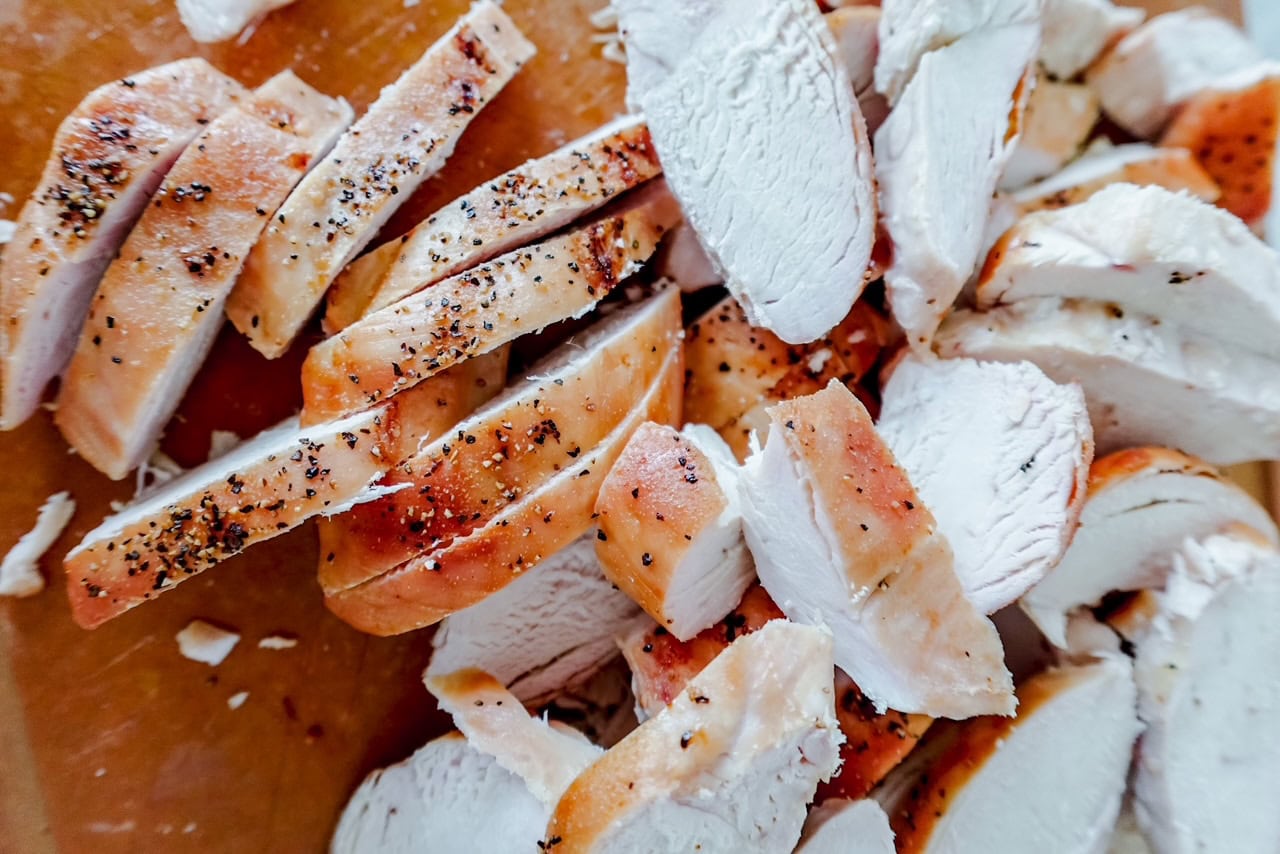 closeup overhead view of chopped, cooked chicken breast pieces seasoned with pepper on a cutting board