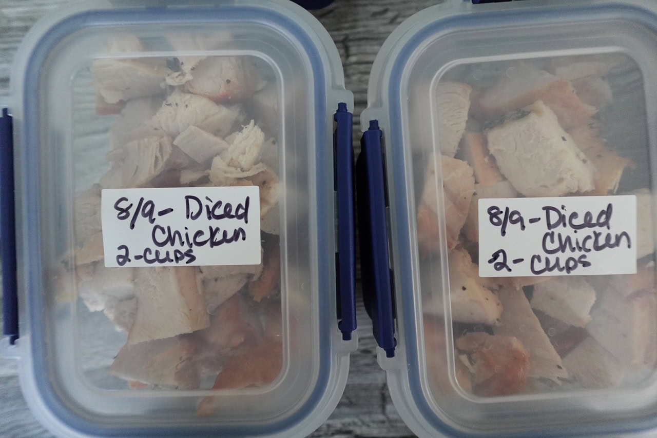 overhead view of two containers with cut cooked chicken inside. On the lids of each container is written "8/9 - diced chicken 2-cups"