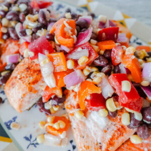Grilled salmon fillets topped with a colorful salsa of black beans, corn, diced tomatoes, red onions, and bell peppers, served on a decorative plate.