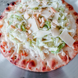 Close-up of the toppings on a Caesar salad-inspired flatbread pizza with lettuce, Parmesan, and crouton pieces.