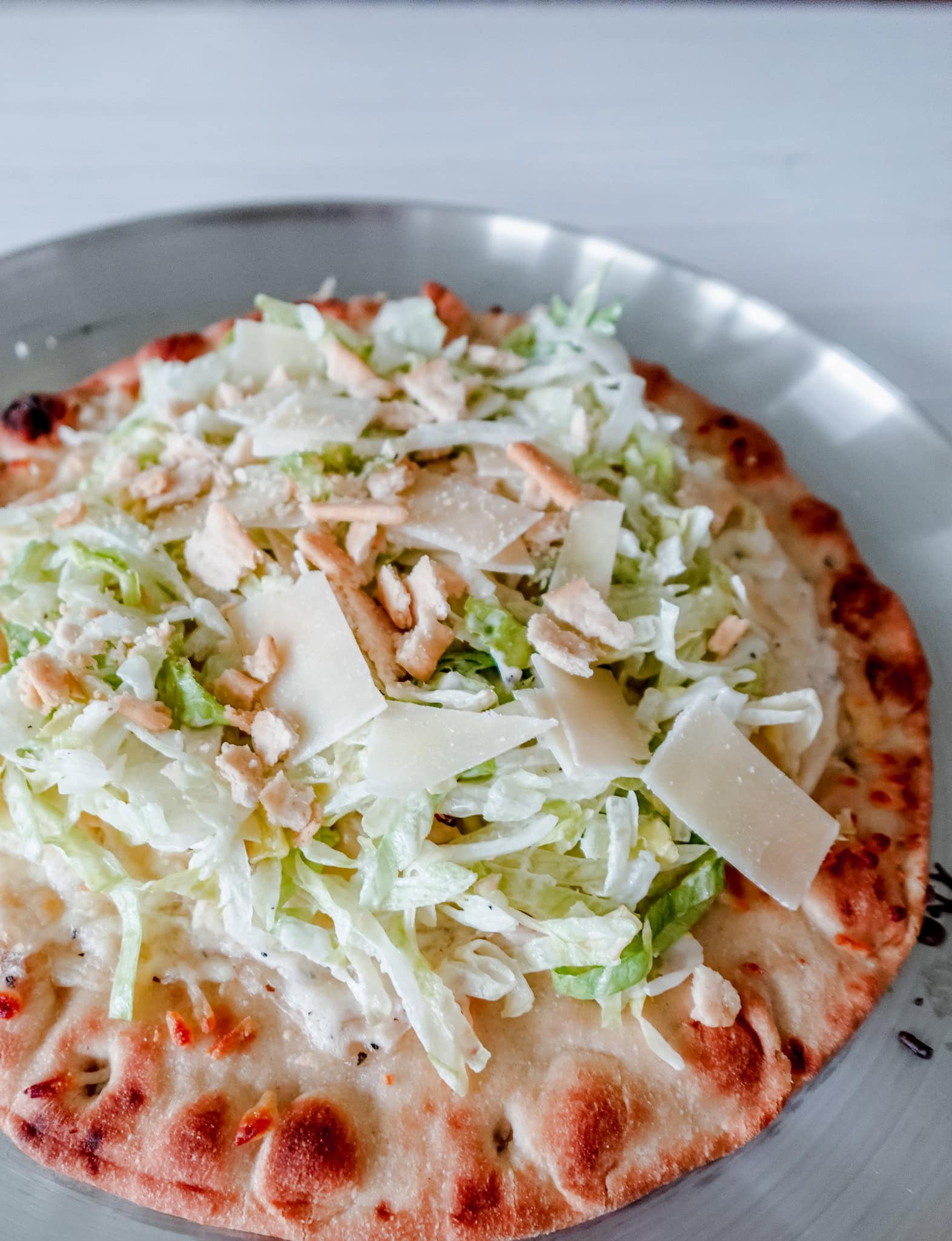 Close-up of the toppings on a Caesar salad-inspired flatbread pizza with lettuce, Parmesan, and crouton pieces.