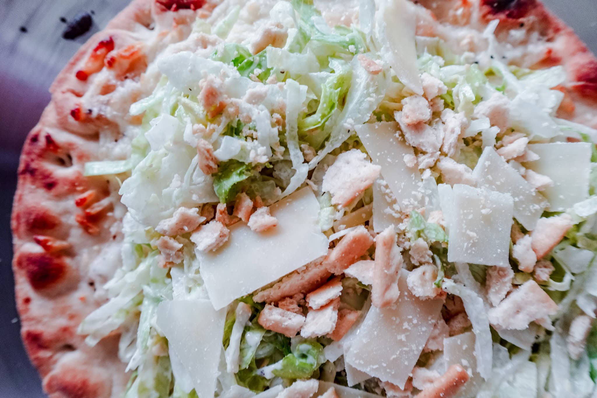 Close-up of the toppings on a Caesar salad-inspired flatbread pizza with lettuce, Parmesan, and crouton pieces.