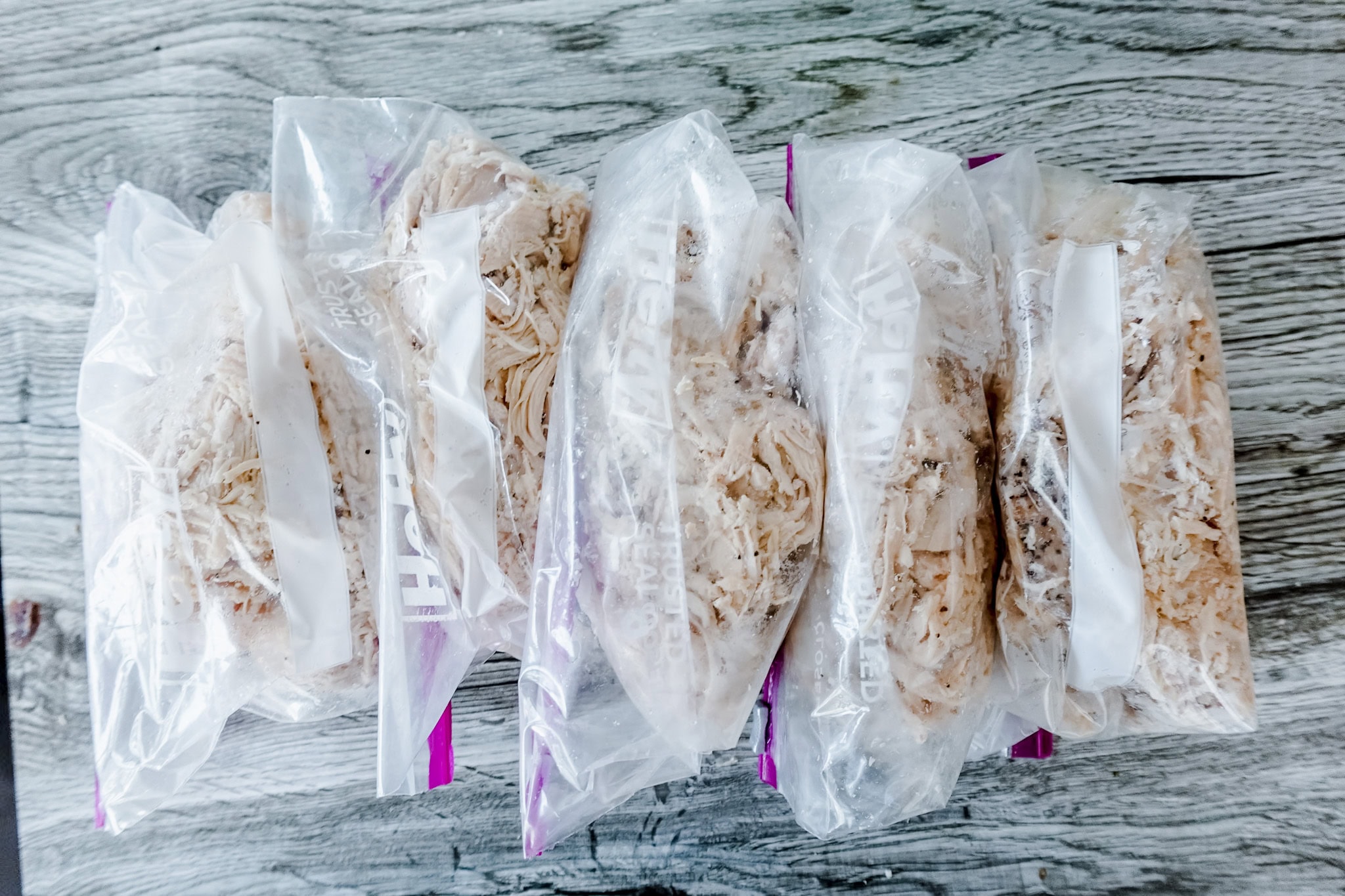 An overview shot of 5 resealable baggies with seasoned shredded chicken sitting on a gray wooden table.