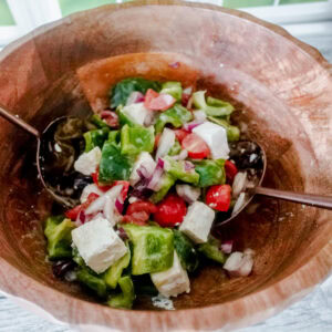 A wooden bowl filled with a fresh, colorful salad containing chopped green peppers, cherry tomatoes, red onion, and chunks of feta cheese.