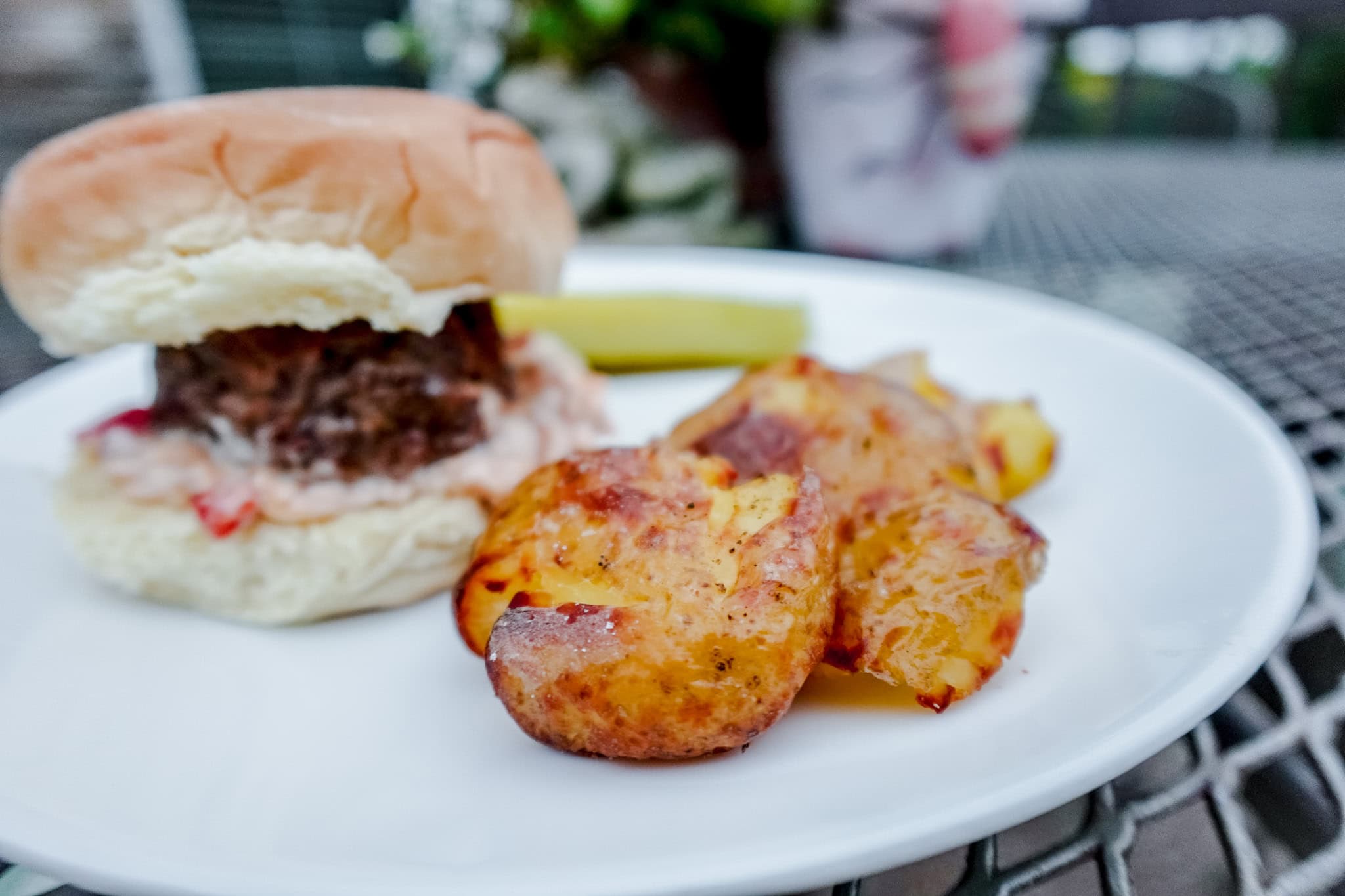 A delicious burger with a fluffy bun, topped with sauce, served with crispy roasted potatoes and a pickle on the side.