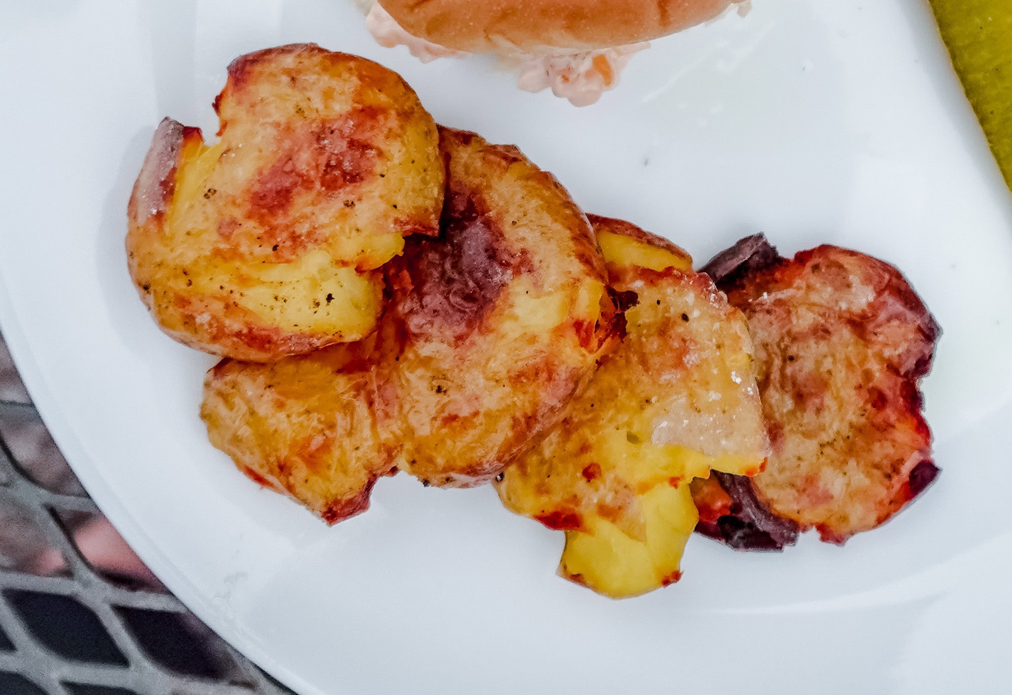 A plate with cheesy golden-brown crispy potato slices, garnished and ready to be served, alongside a sandwich and pickle.