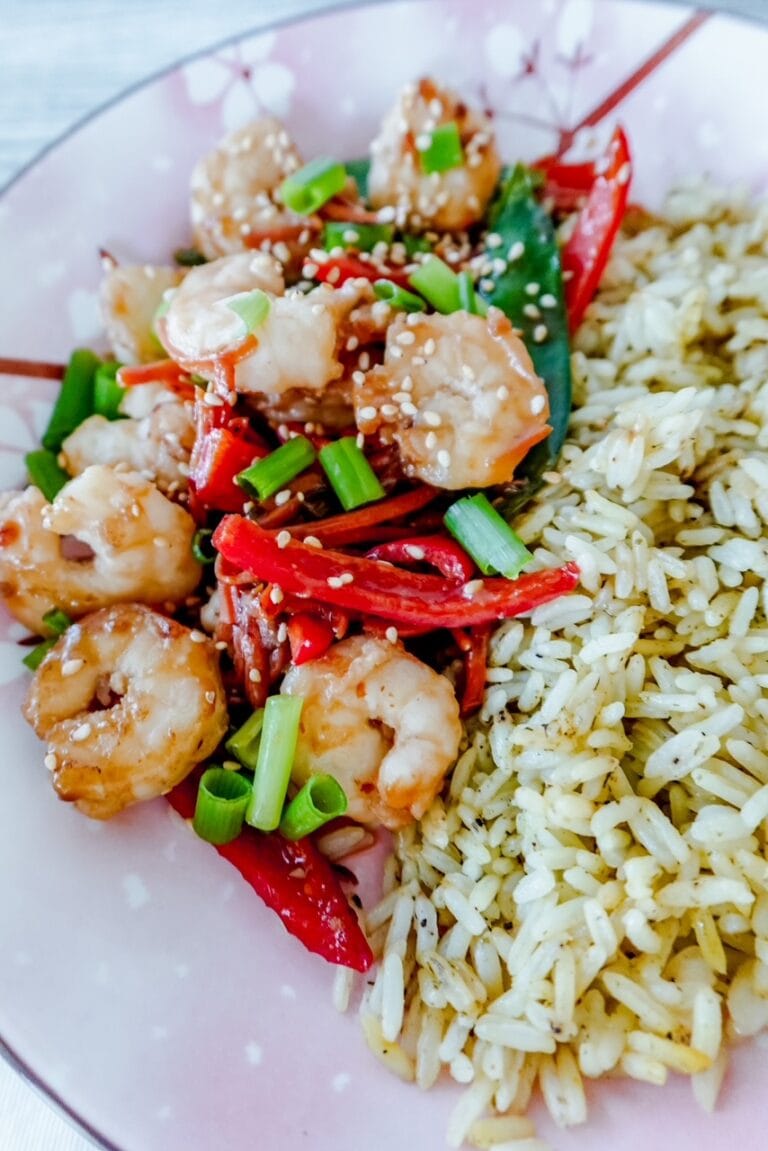 Stir-fried shrimp with sesame seeds, red peppers, and green onions, paired with seasoned rice on a floral-patterned pink plate.