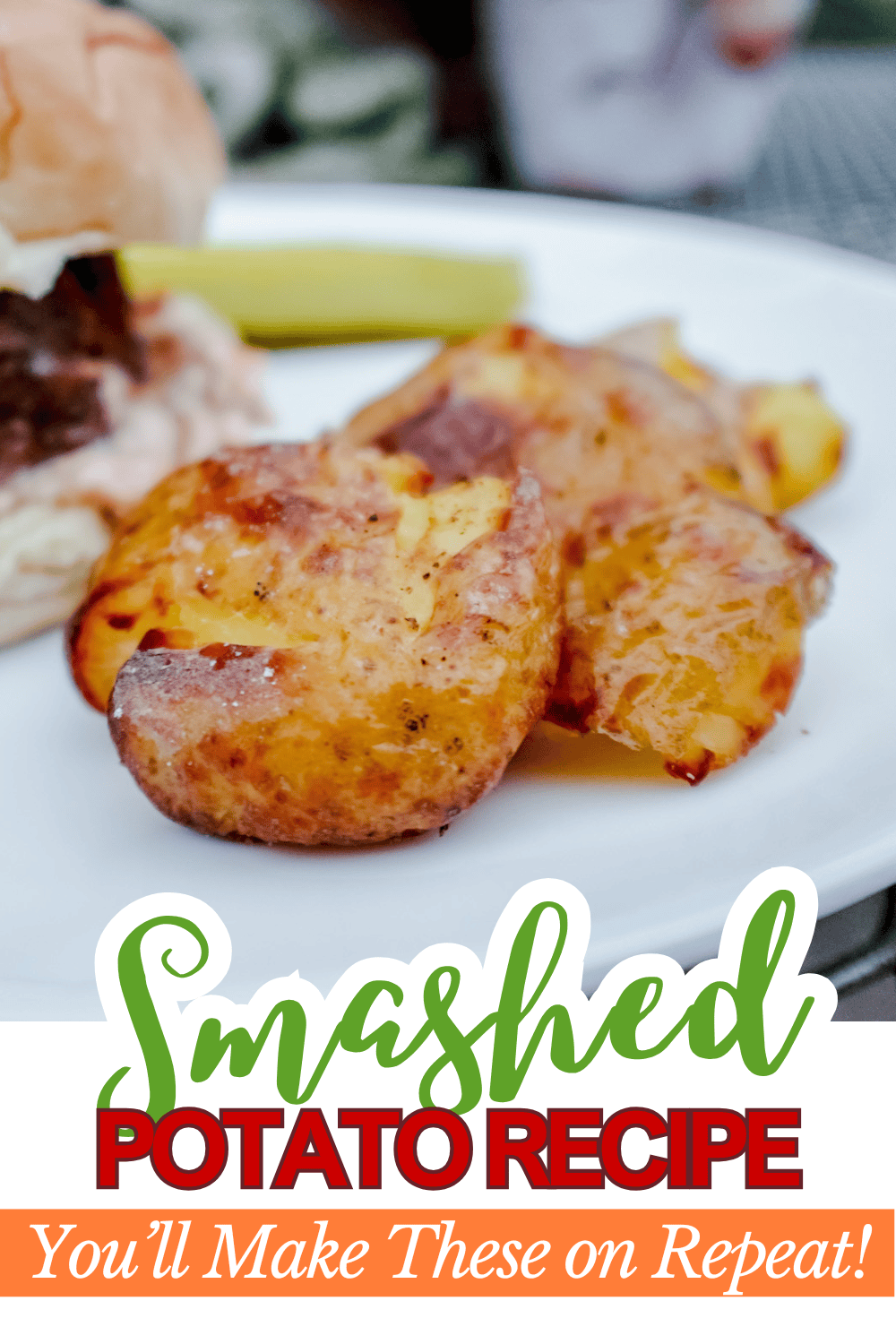 A close-up of crispy smashed potatoes on a white plate next to a sandwich and pickle. The text overlay reads: Smashed Potato Recipe - Youll Make These on Repeat!.
