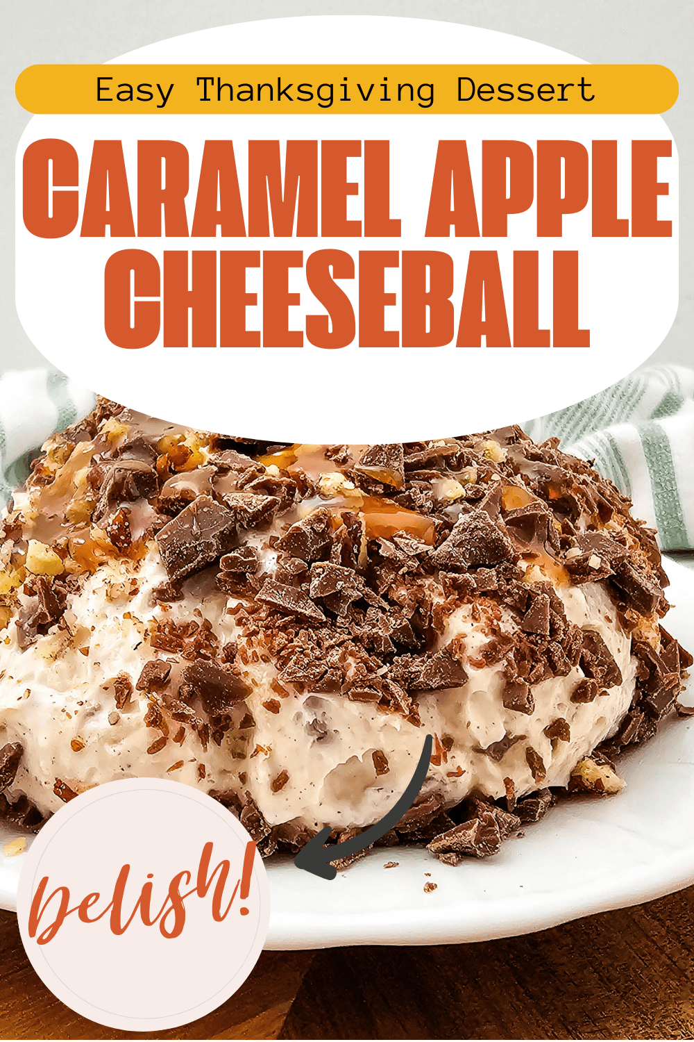 A caramel apple cheeseball covered in chocolate shavings sits on a white plate. The image text reads: Easy Thanksgiving Dessert. Caramel Apple Cheeseball. Delish! with a striped cloth in the background.