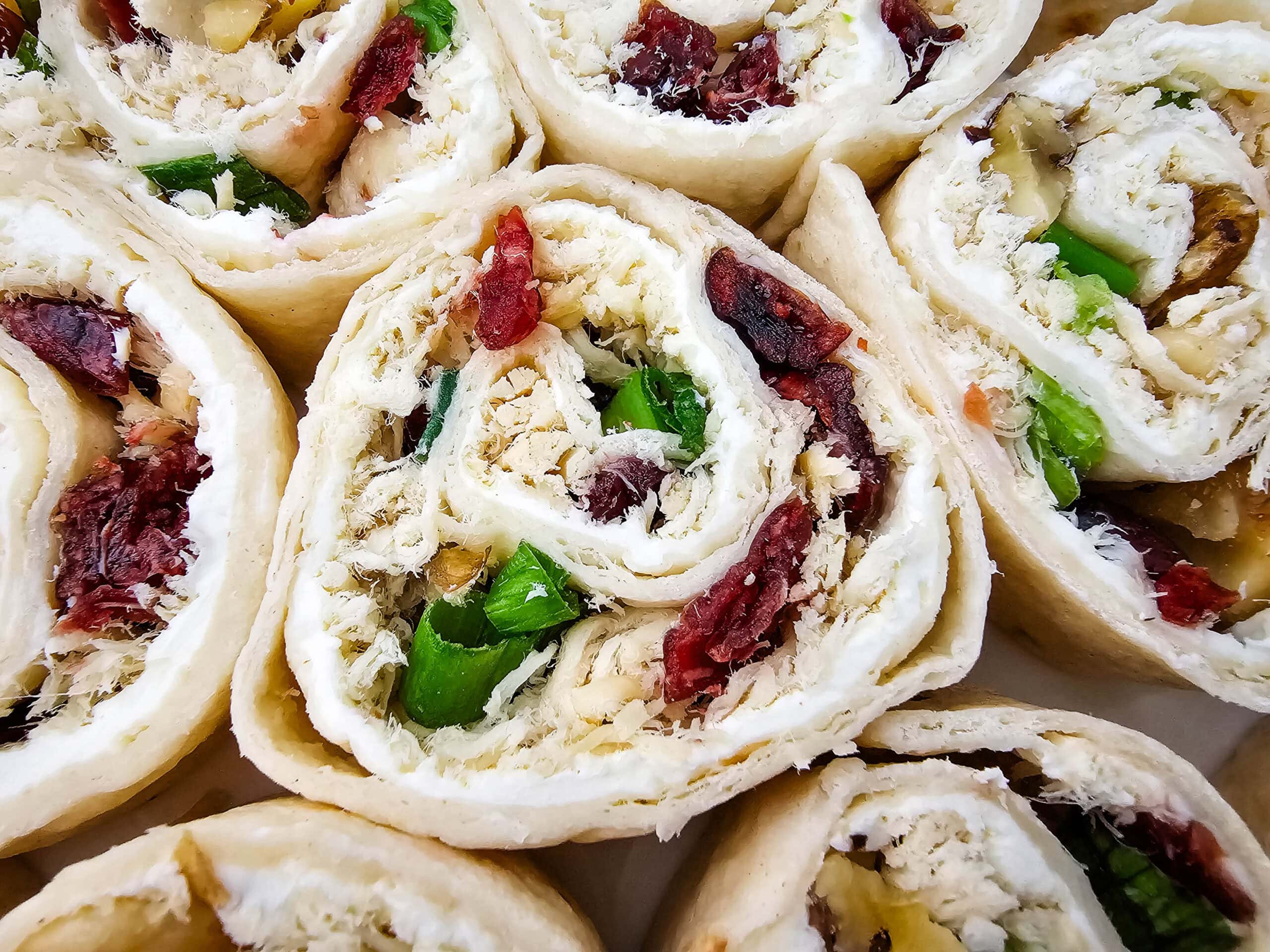 Close-up of several tortilla pinwheels filled with shredded chicken, dried cranberries, green onions, and a creamy spread, arranged tightly together.