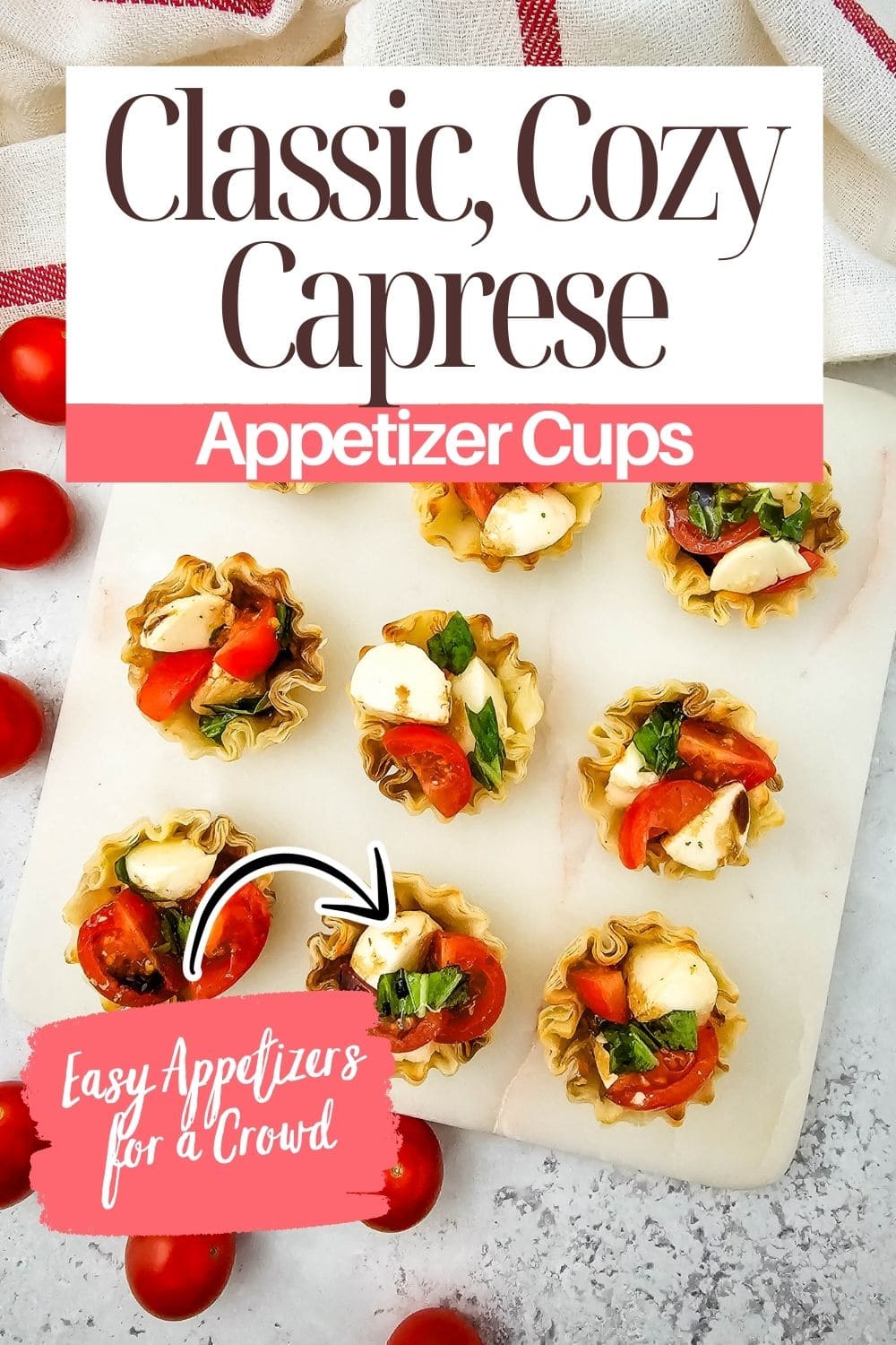 Overhead view of nine caprese appetizer cups with tomatoes, mozzarella, and basil on a white board, surrounded by cherry tomatoes. Text reads: Classic, Cozy Caprese Appetizer Cups; Easy Appetizers for a Crowd.