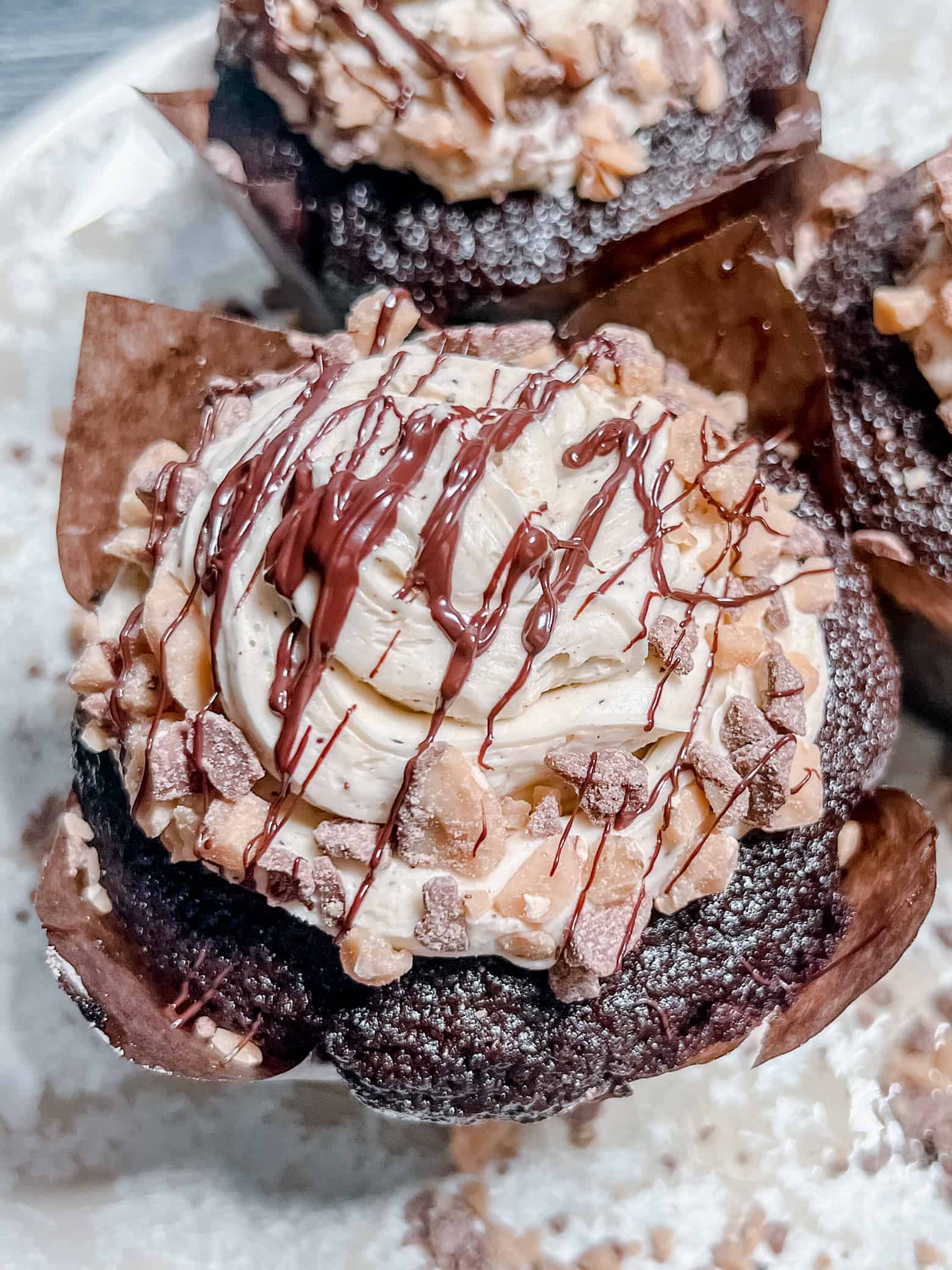 A close-up of a chocolate cupcake topped with swirled frosting, chopped nuts, and a drizzle of chocolate in a brown paper liner—perfect for savoring those Snug and Cozy Life moments.