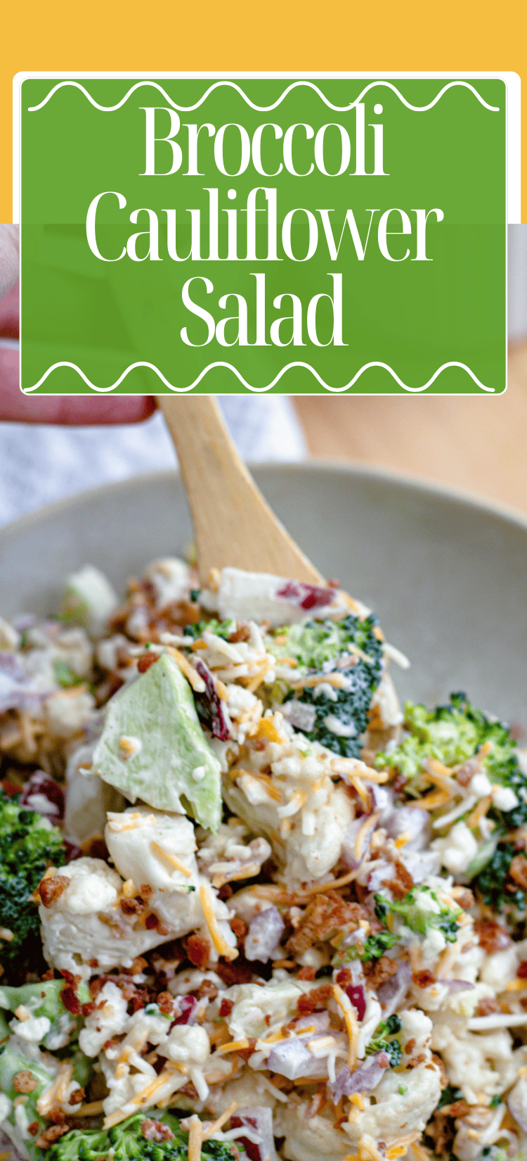A close-up of a bowl of broccoli cauliflower salad with shredded cheese, bacon bits, and red onion, being mixed with a wooden spoon. Text above the image reads: Broccoli Cauliflower Salad.