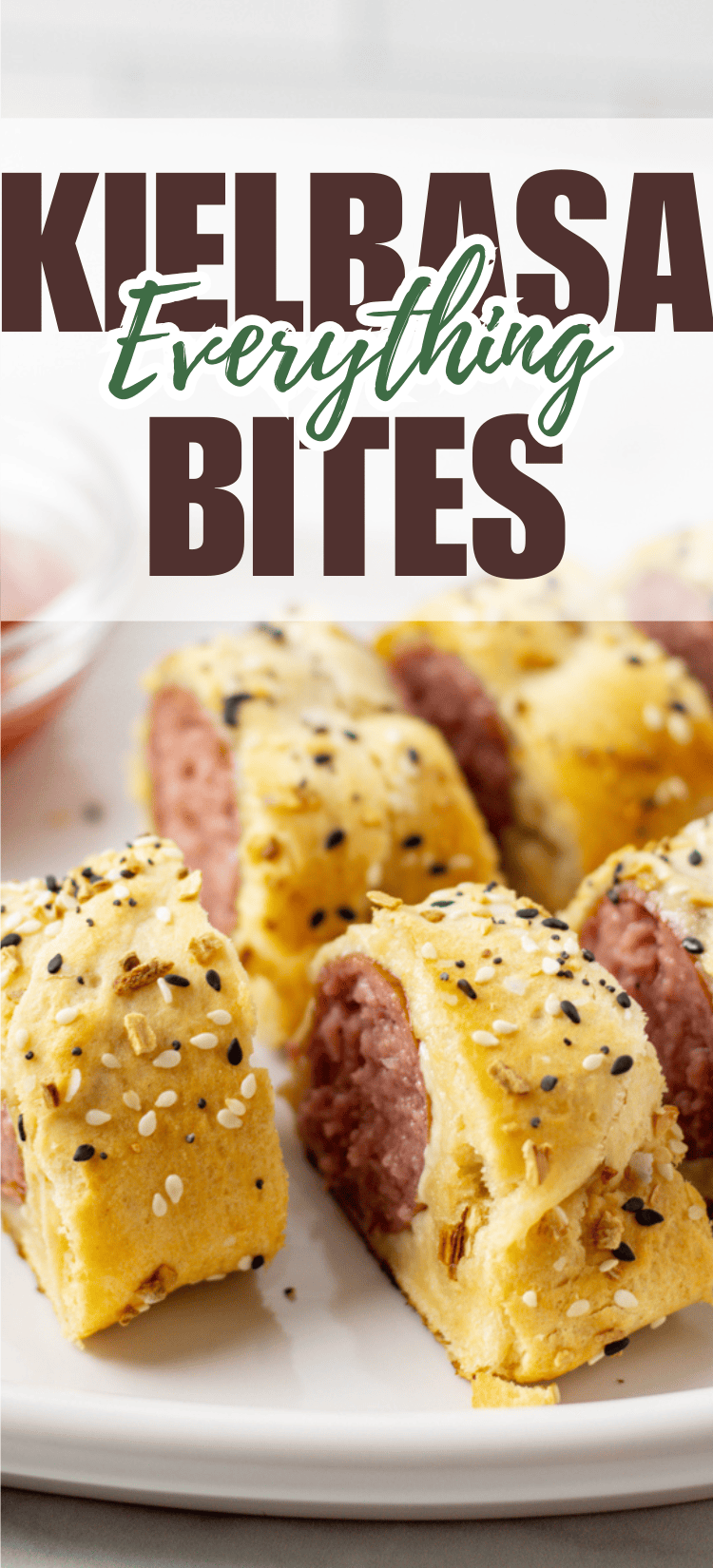 Close-up of sliced kielbasa sausage wrapped in golden baked dough, topped with sesame and poppy seeds, arranged on a white plate. Text overlay reads “Kielbasa Everything Bites.”.