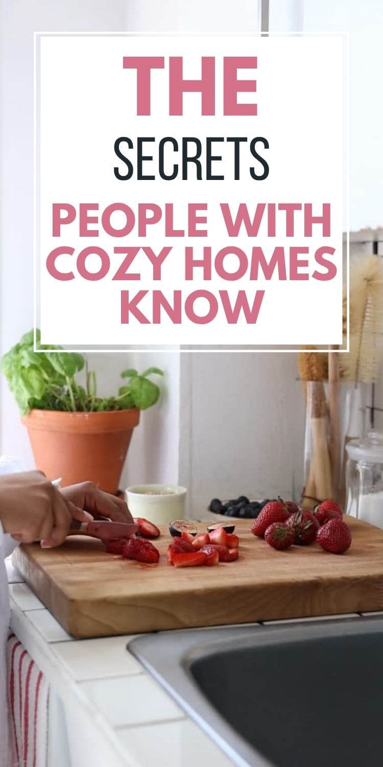 A person slicing strawberries on a wooden cutting board in a bright, cozy kitchen with plants and utensils in the background. Text overlay reads: The secrets people with cozy homes know.