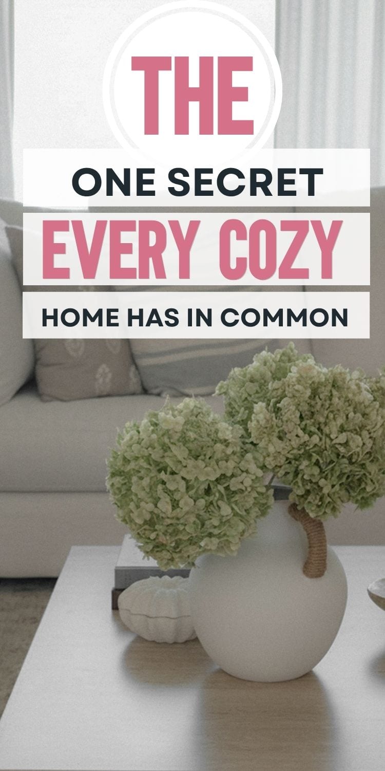 A white vase with green hydrangeas sits on a coffee table in front of a beige sofa. Overlaid text reads: The one secret every cozy home has in common.
