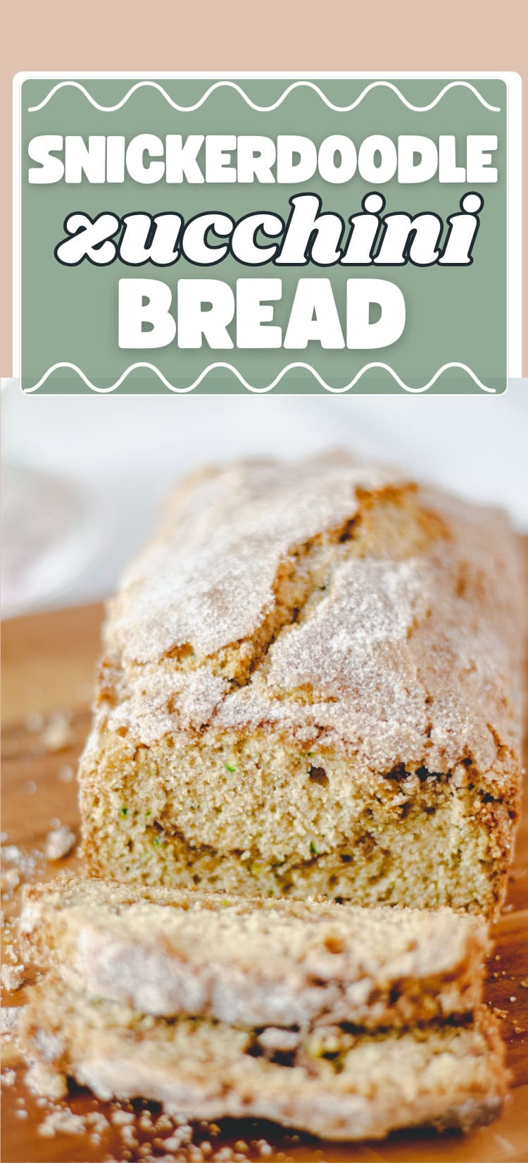 A loaf of snickerdoodle zucchini bread dusted with sugar, sitting on a wooden board with a few slices cut in front. Above the bread is a decorative sign reading “Snickerdoodle Zucchini Bread.”.