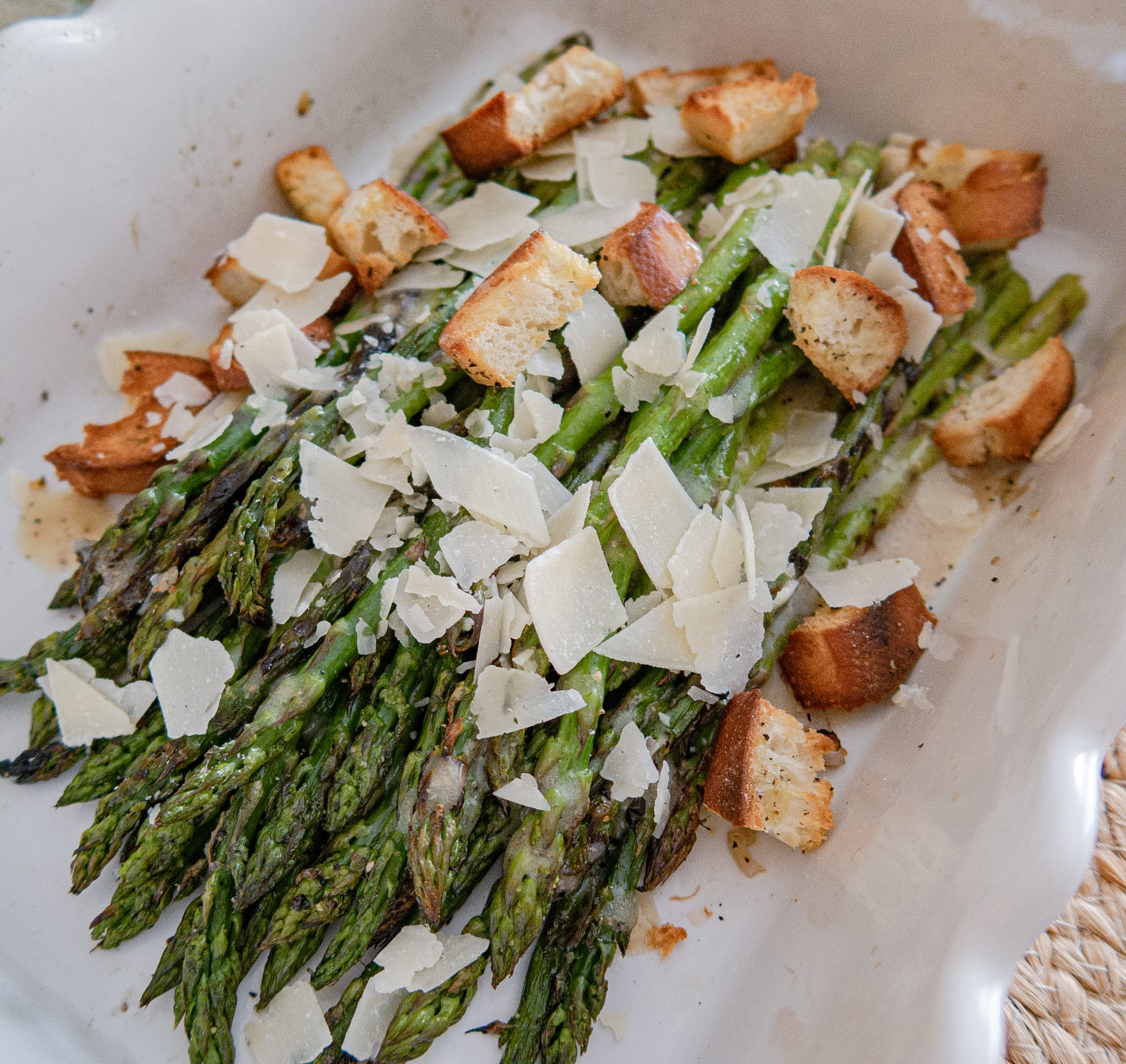 Roasted asparagus spears topped with shaved Parmesan cheese and golden brown croutons, served in a white ceramic dish.